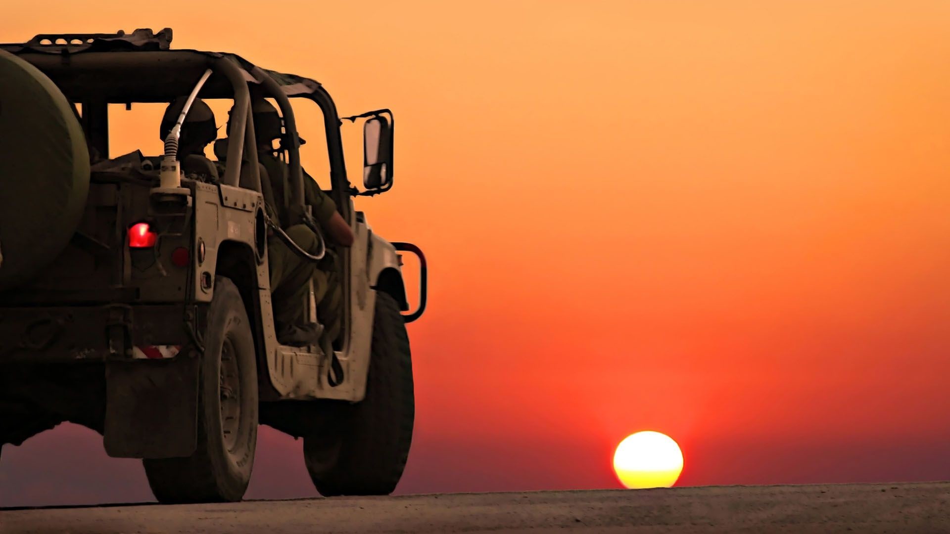 Silhouetted military vehicle against a vibrant sunset backdrop