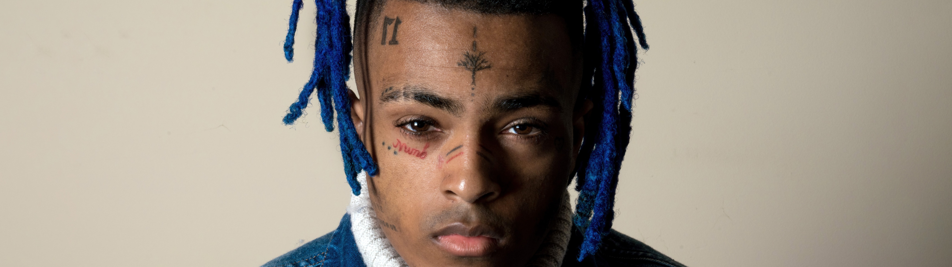 Close-up portrait of XXXTentacion with blue dreadlocks, showcasing his facial tattoos