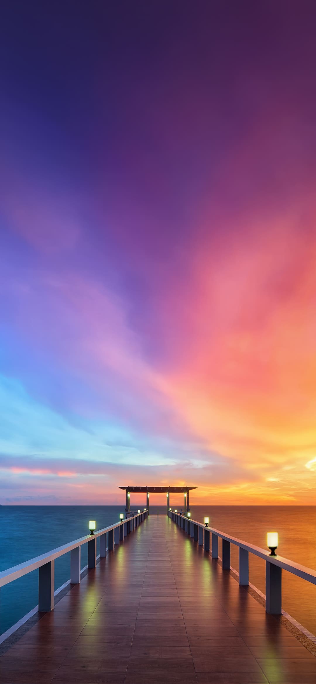A wooden pier stretches out into the ocean under a vibrant sunset sky