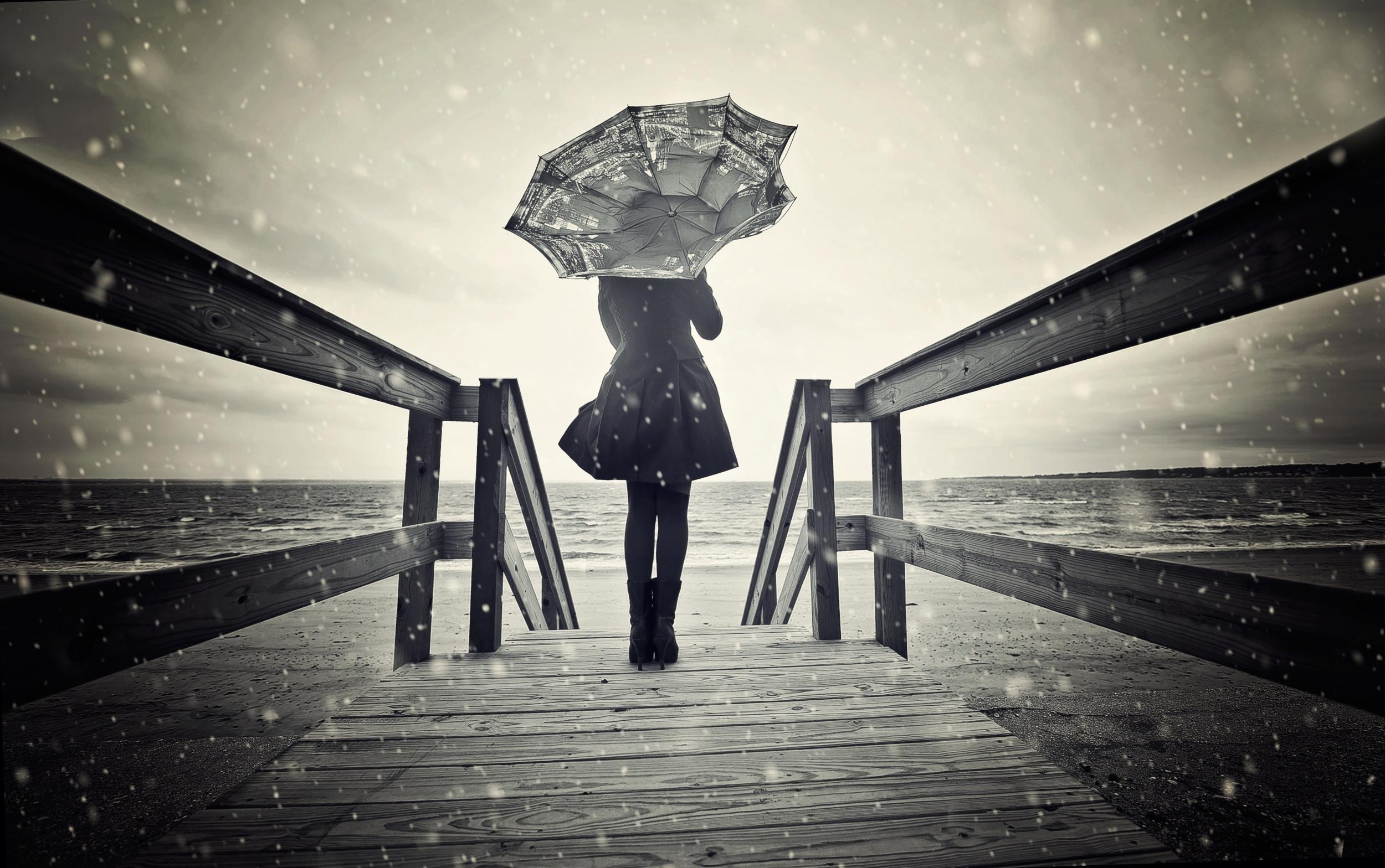 A lone figure stands at the end of a wooden pier under a dark, snowy sky, gazing out at the turbulent sea, evoking a sense of melancholy and introspection