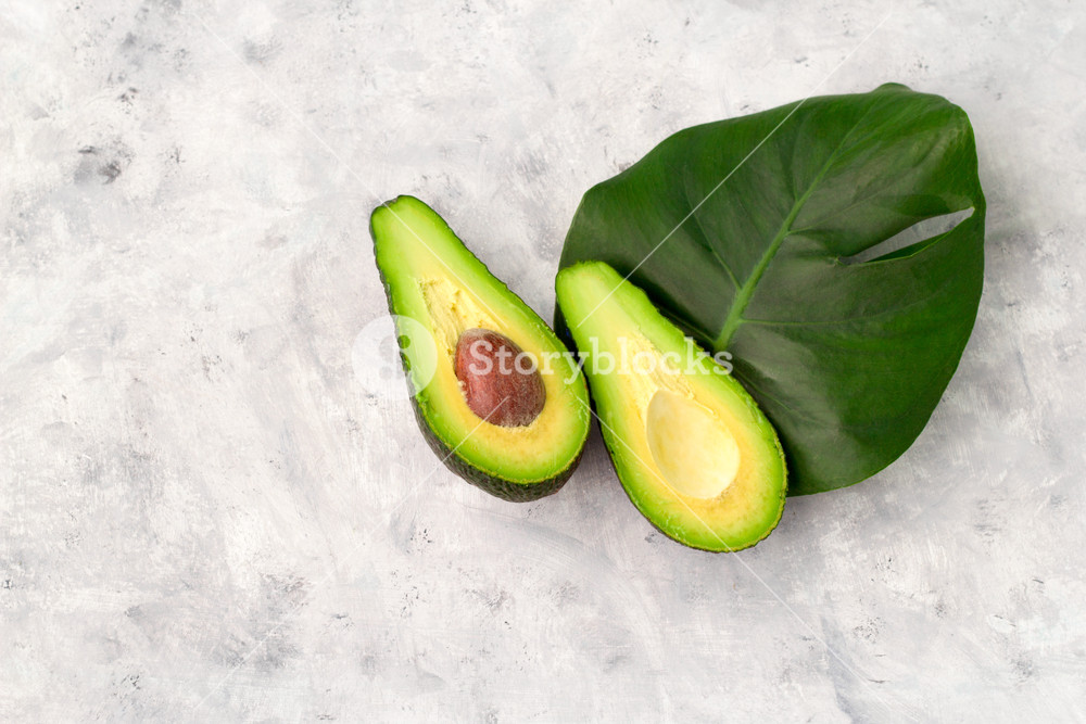 Top Of Halved Avocado And Monstera Leaf On A Gray Background