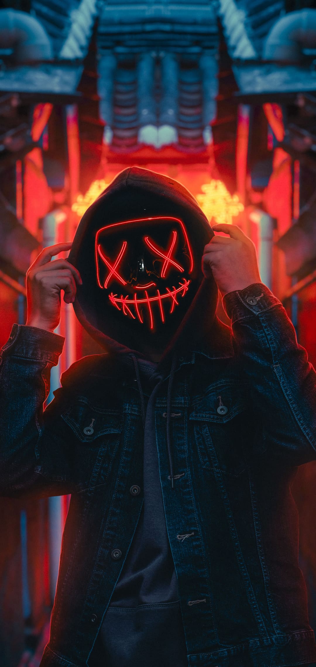 Person wearing a glowing red mask and denim jacket in a dark urban setting, suitable for a cool phone wallpaper