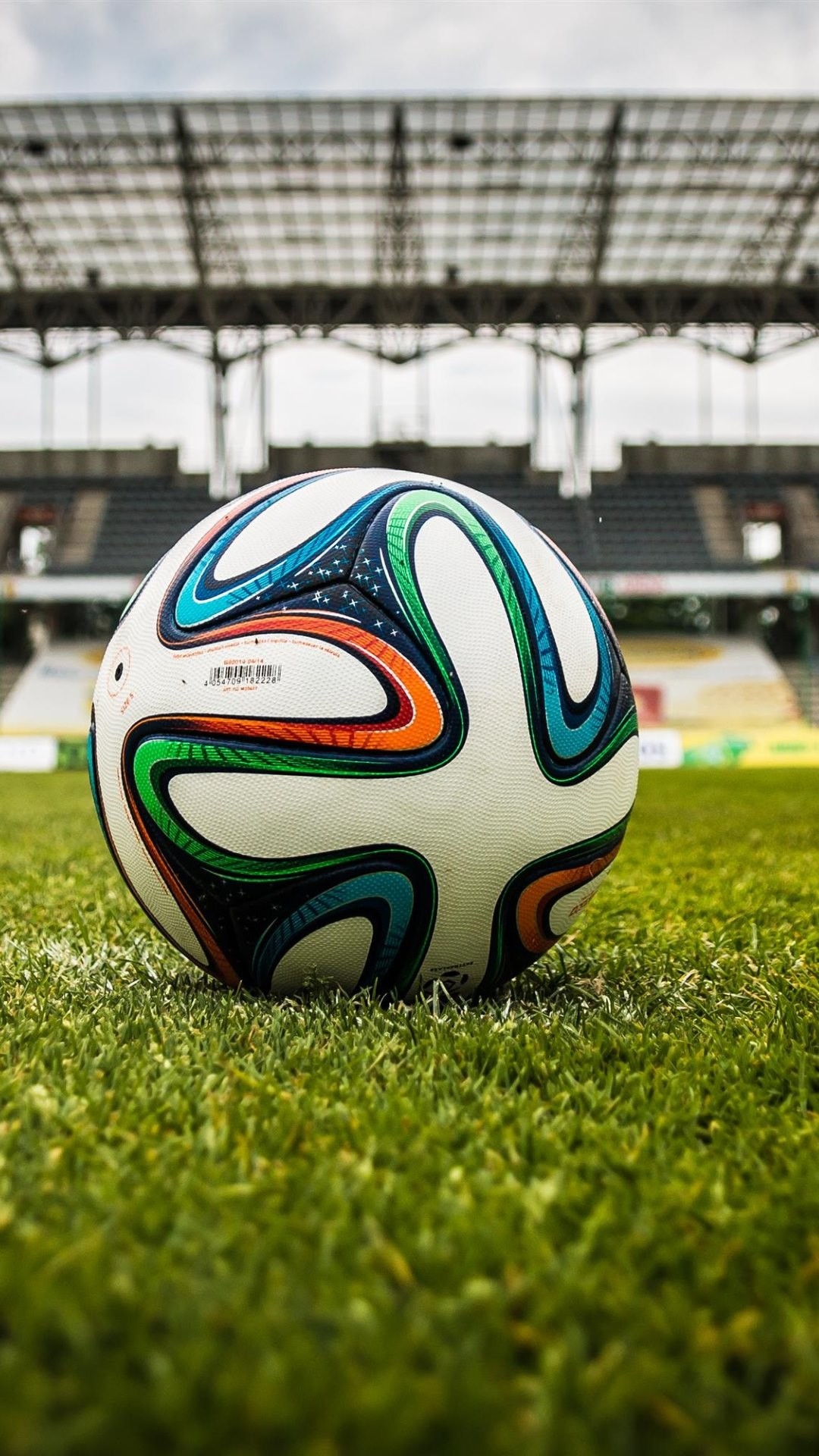 A vibrant soccer ball sits on a lush green field in a stadium, ready for action