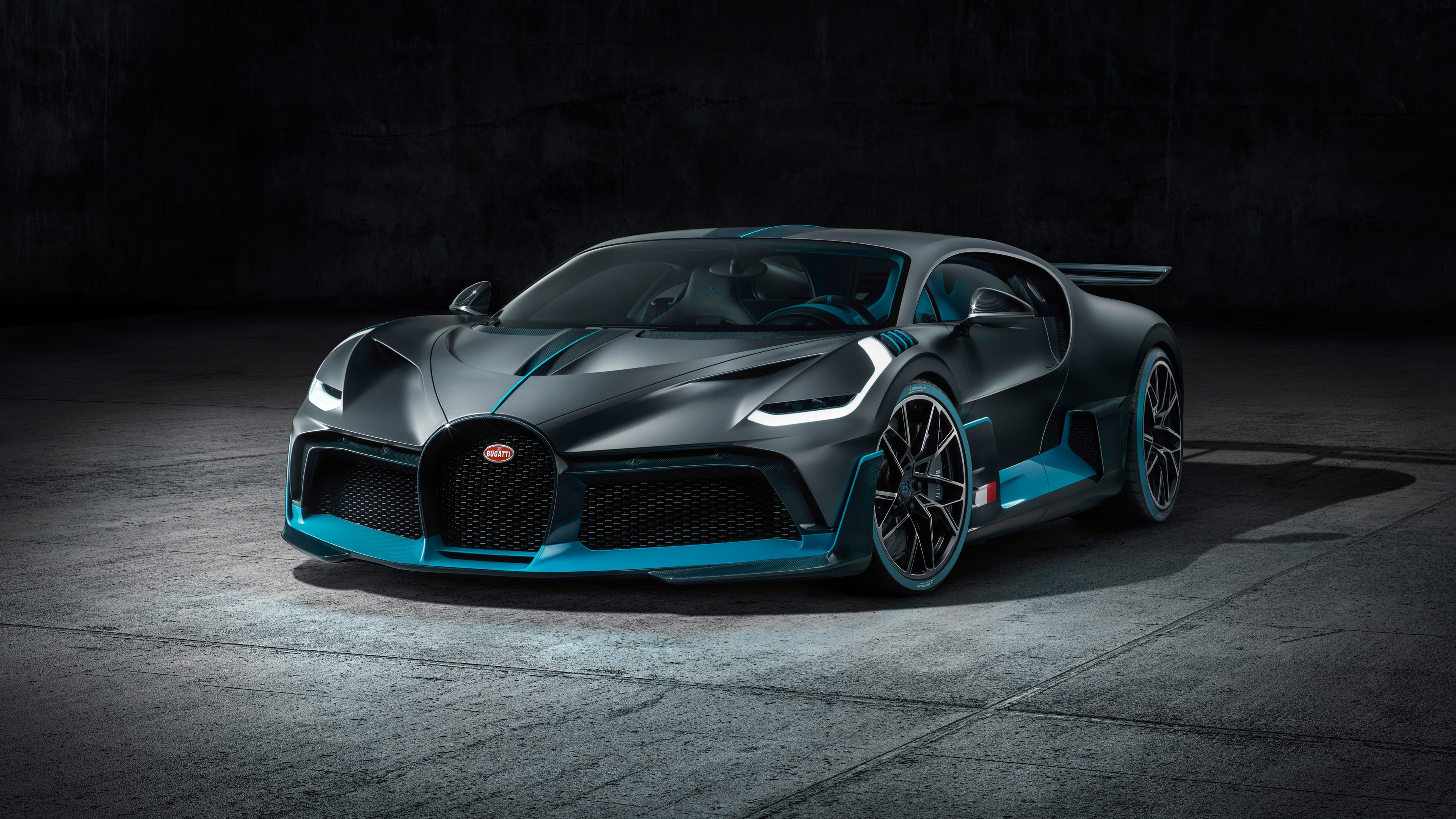 A sleek, dark gray Bugatti Chiron Super Sport with vibrant teal accents, parked on a polished concrete floor under dramatic lighting