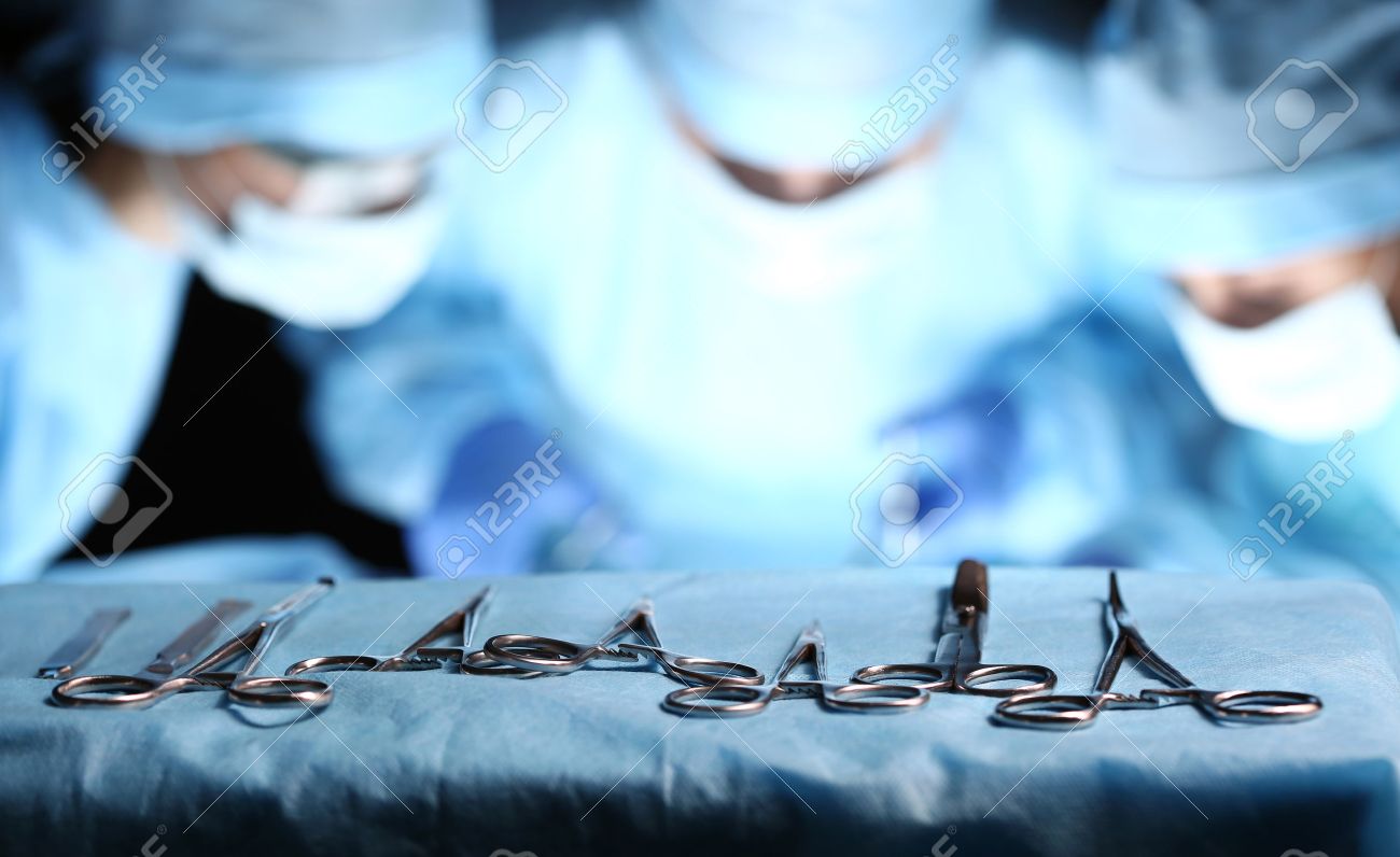 Surgical Tools Lying On Table Wile Group Of Surgeons At Background