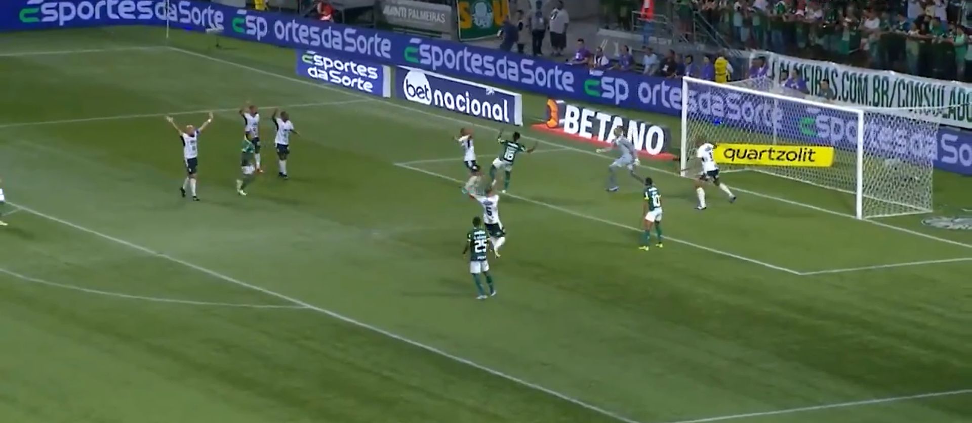A soccer game in progress with players from both teams on the field. The ball is near the goal, and some players are celebrating