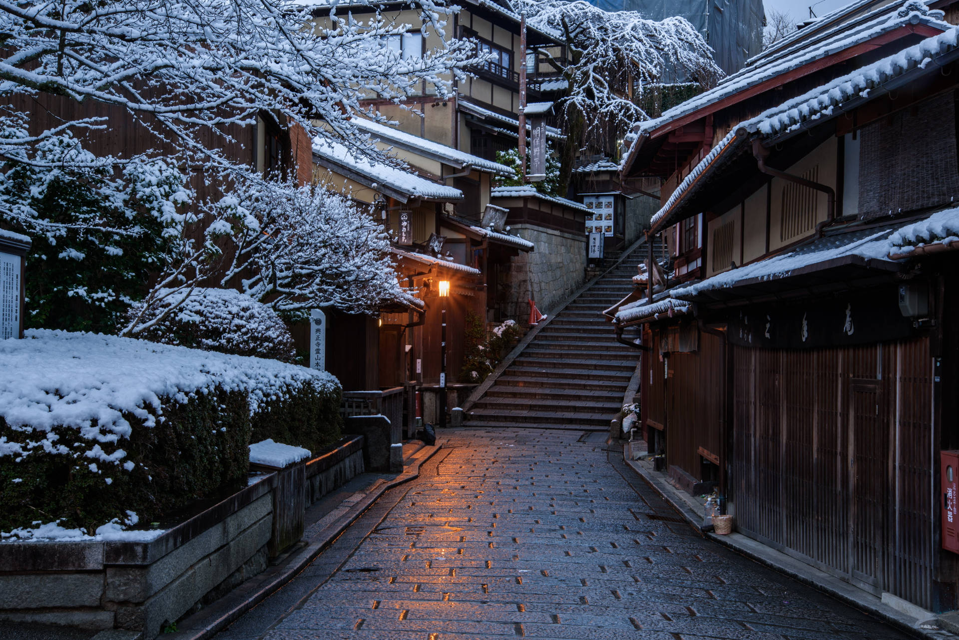A serene 4k wallpaper of a snow-dusted Japanese street at dawn, featuring traditional wooden buildings and a warm glow from a street lamp