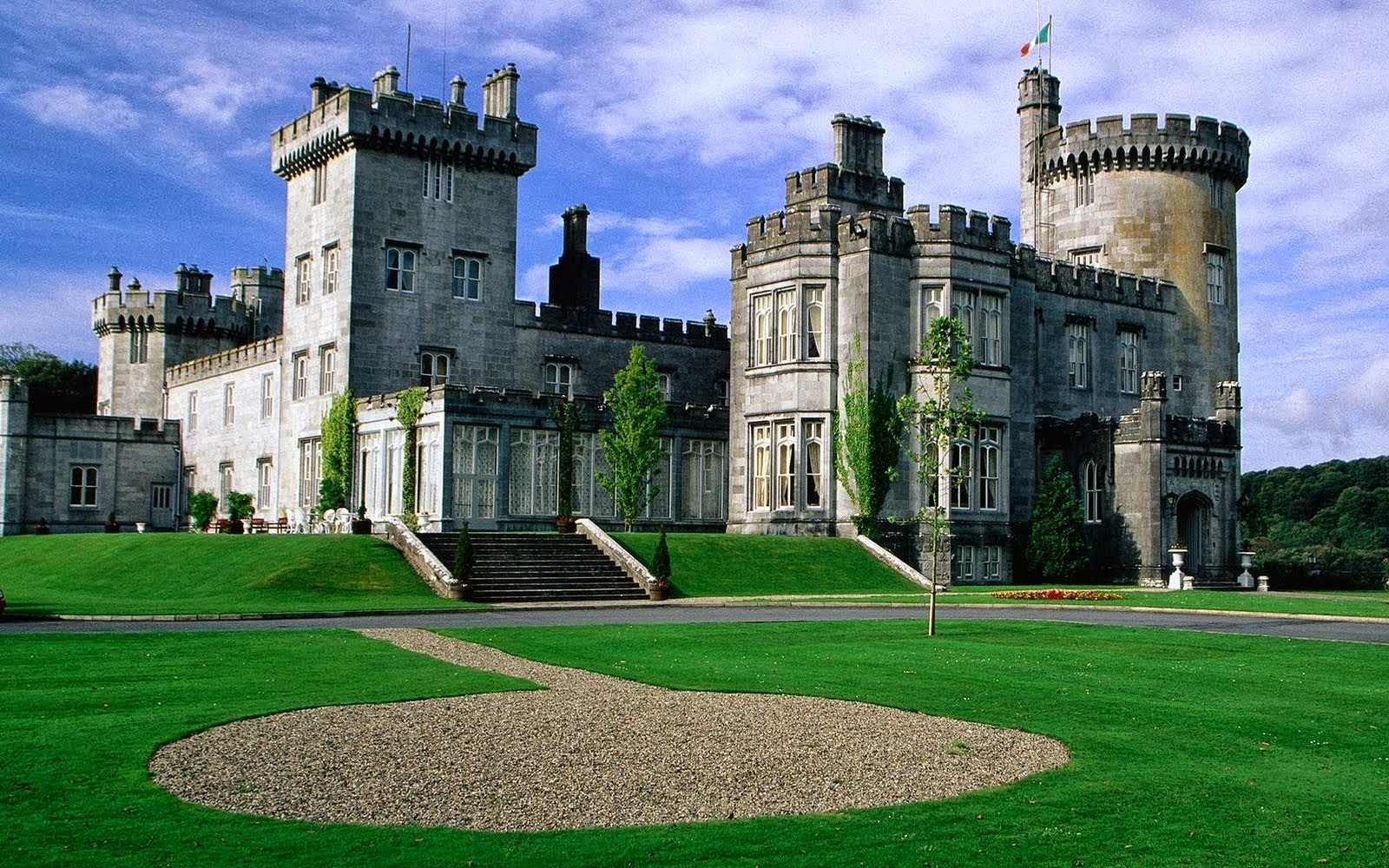 A majestic castle with towers and turrets, set against a clear blue sky, surrounded by lush green lawns