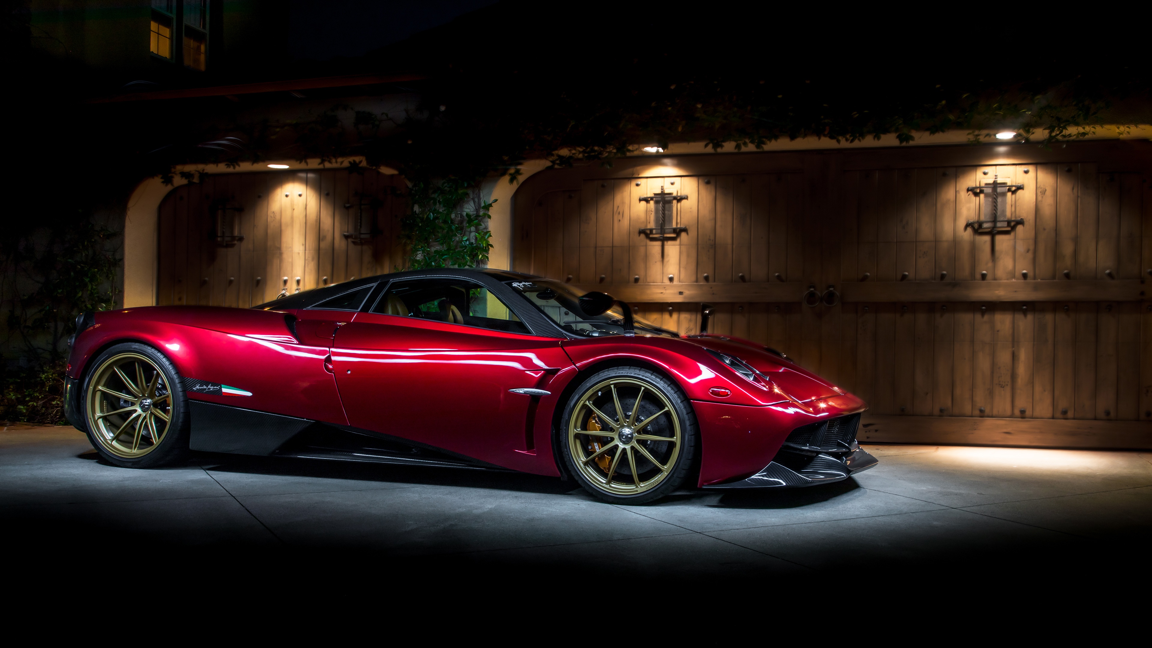 A stunning red Pagani Huayra, parked in front of a wooden garage door at night