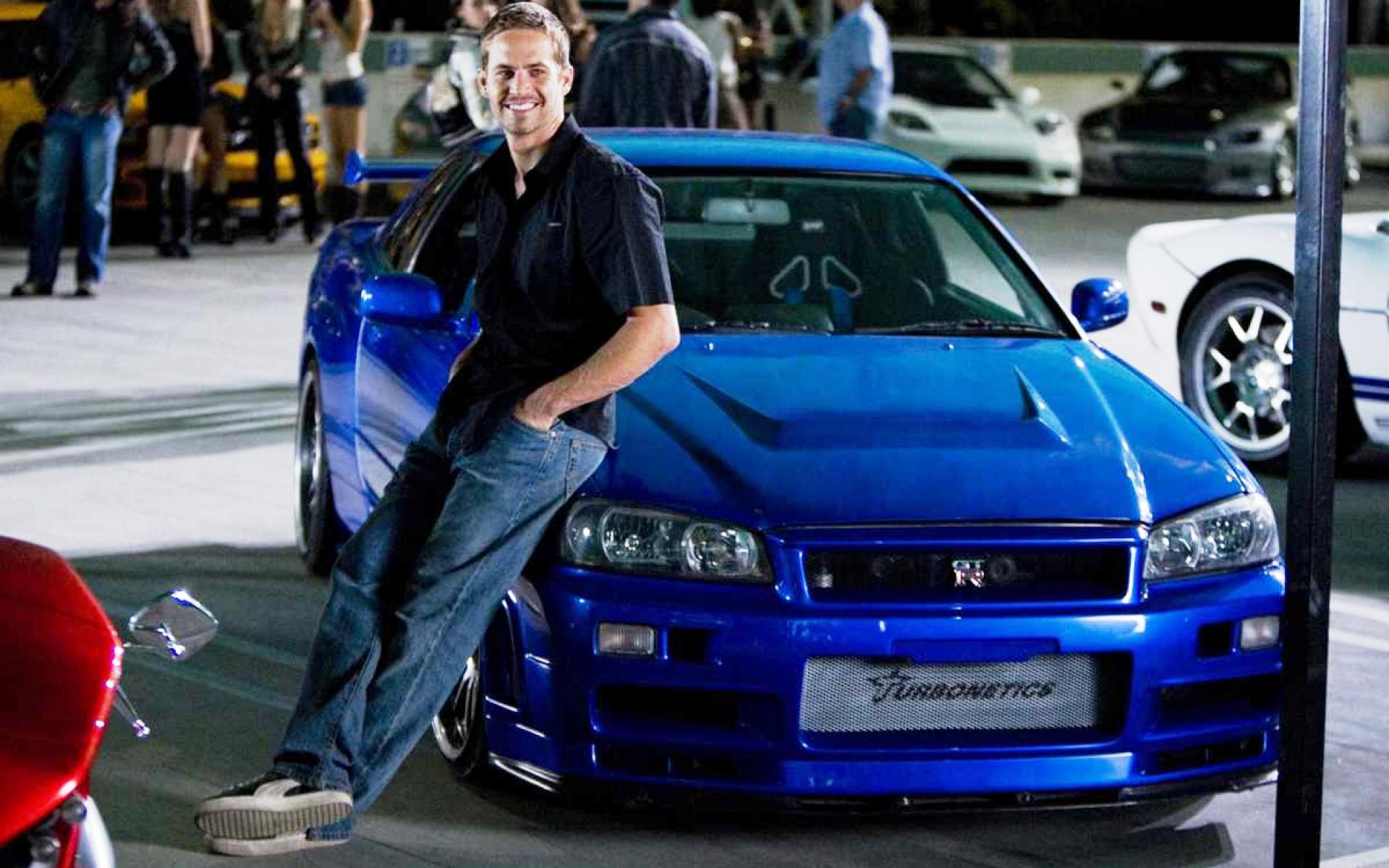 Paul Walker leaning on his iconic blue Nissan Skyline GT-R from the Fast and Furious movie franchise
