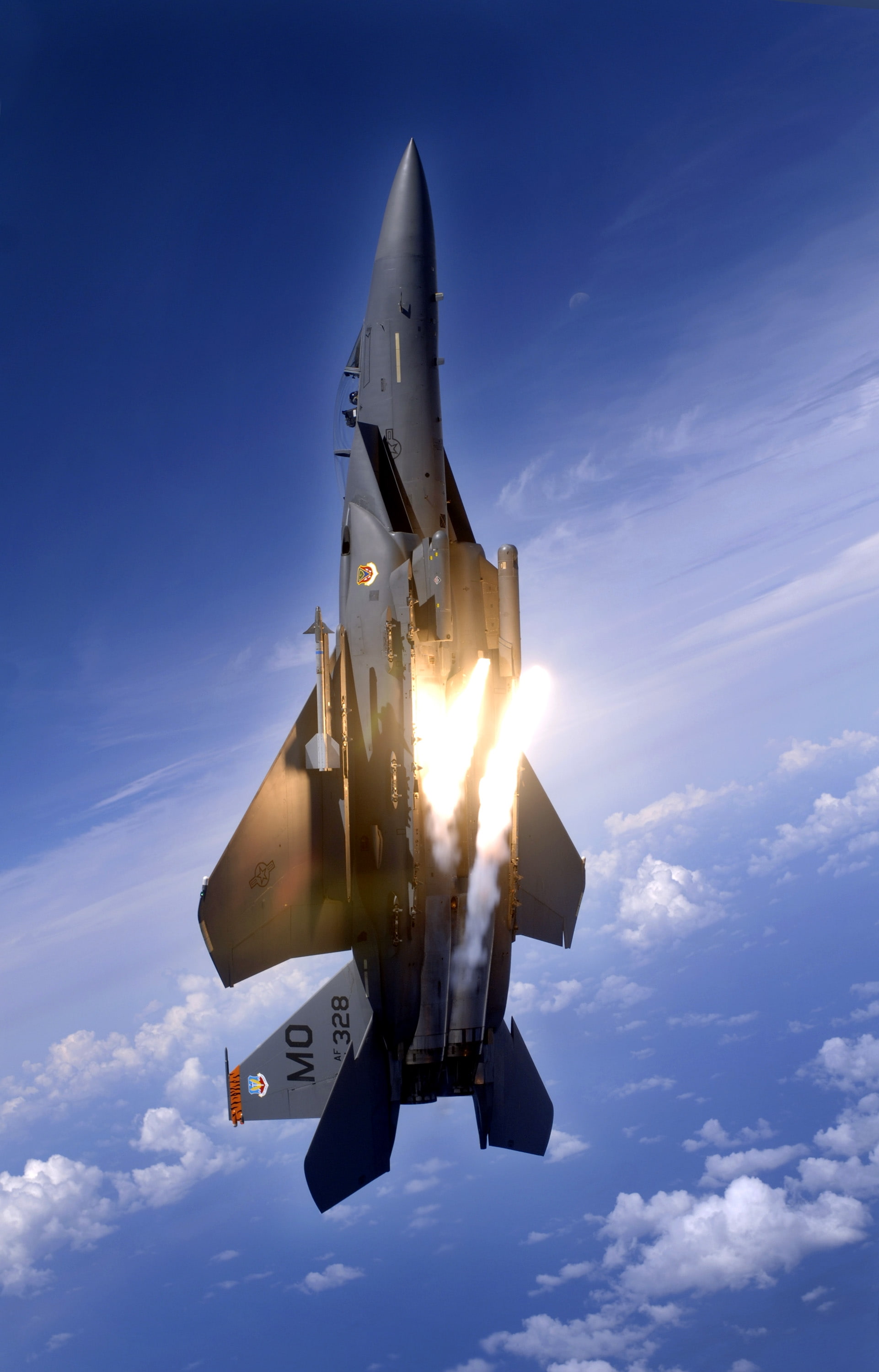 F-15 Eagle releasing flares during a high-G maneuver against a vibrant blue sky
