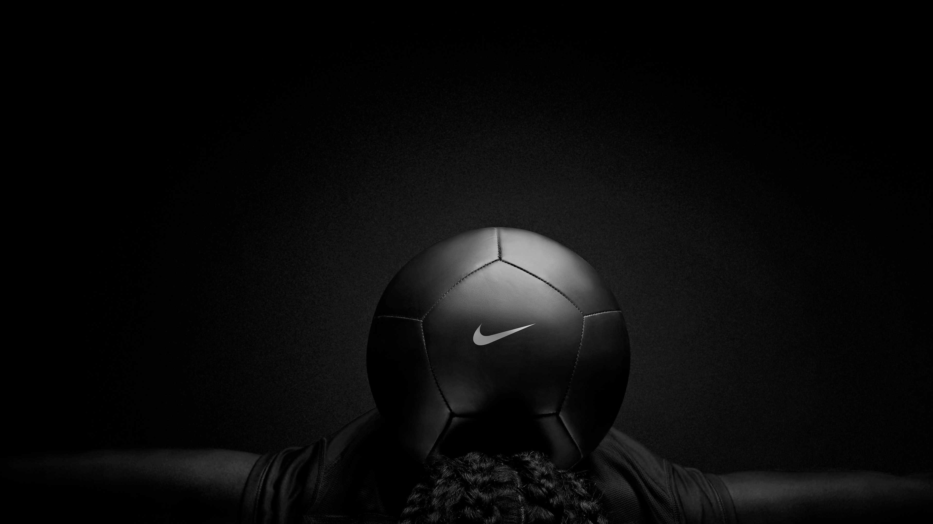 A dramatic black and white image of a Nike football balanced on a person's back against a dark background