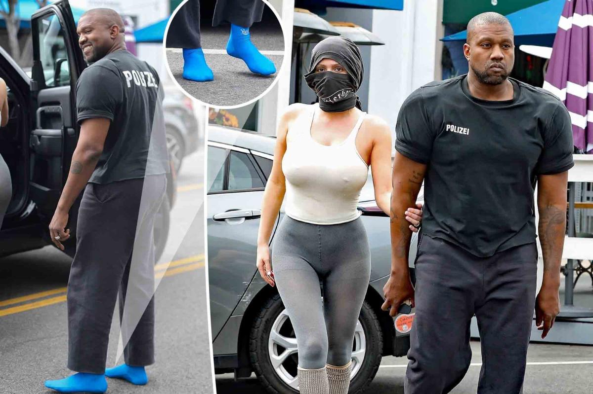 Kanye West and Bianca Censori walking together, with Bianca's face covered by a cloth and Kanye wearing blue socks