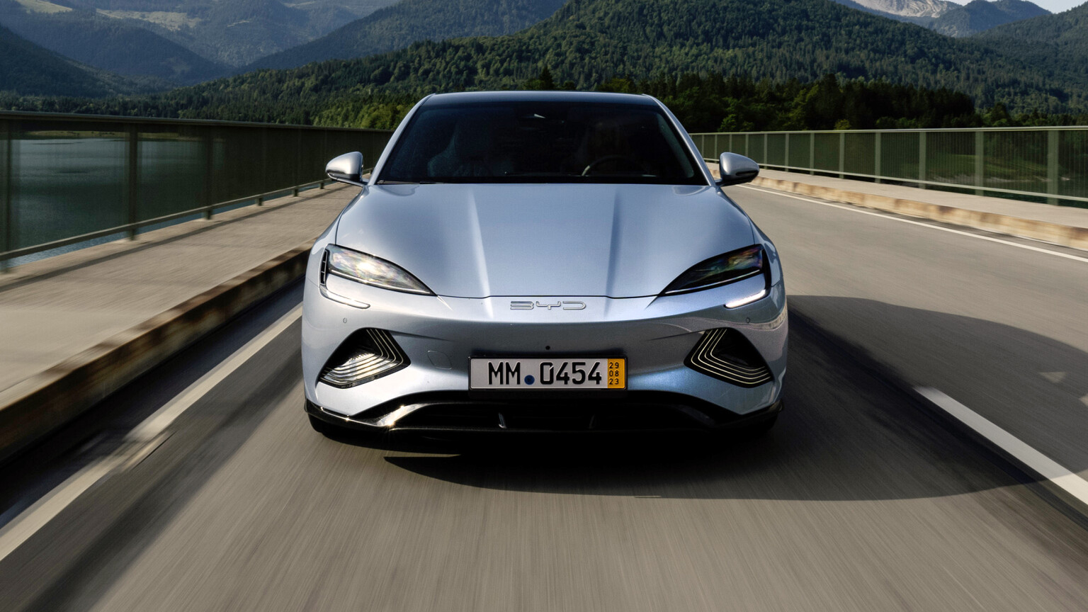 A silver BYD Seal electric car driving on a scenic bridge, showcasing its sleek design and advanced technology