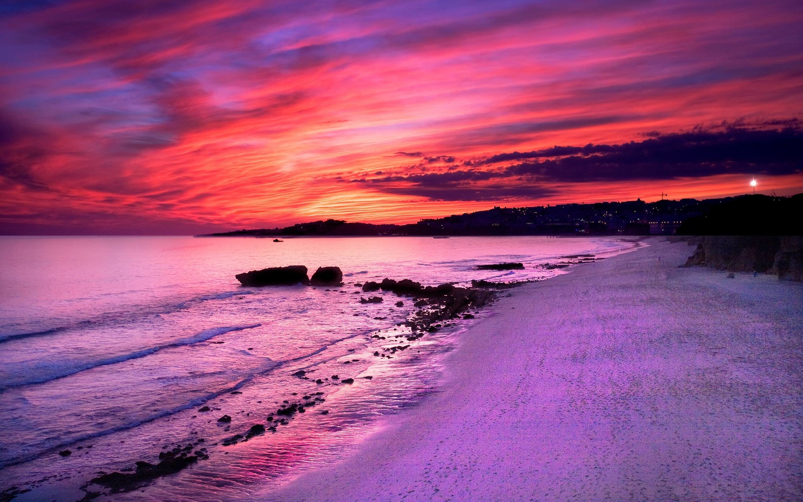 Vivid sunset over a tranquil beach, casting a warm, purple glow on the sand and water