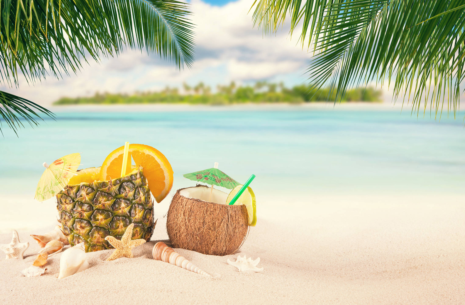 Tropical summer drinks on a sandy beach with palm trees and ocean view