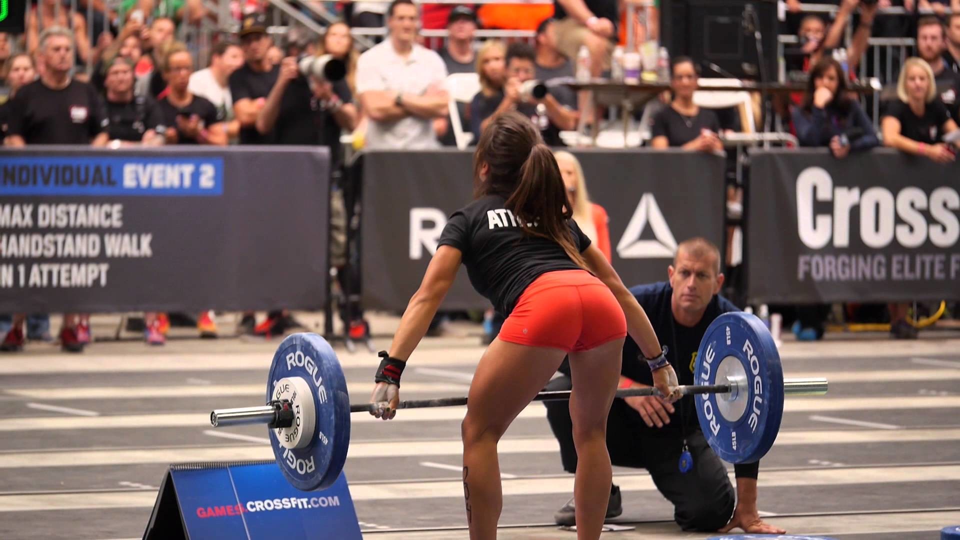 A female CrossFit athlete performing a handstand walk at a competition