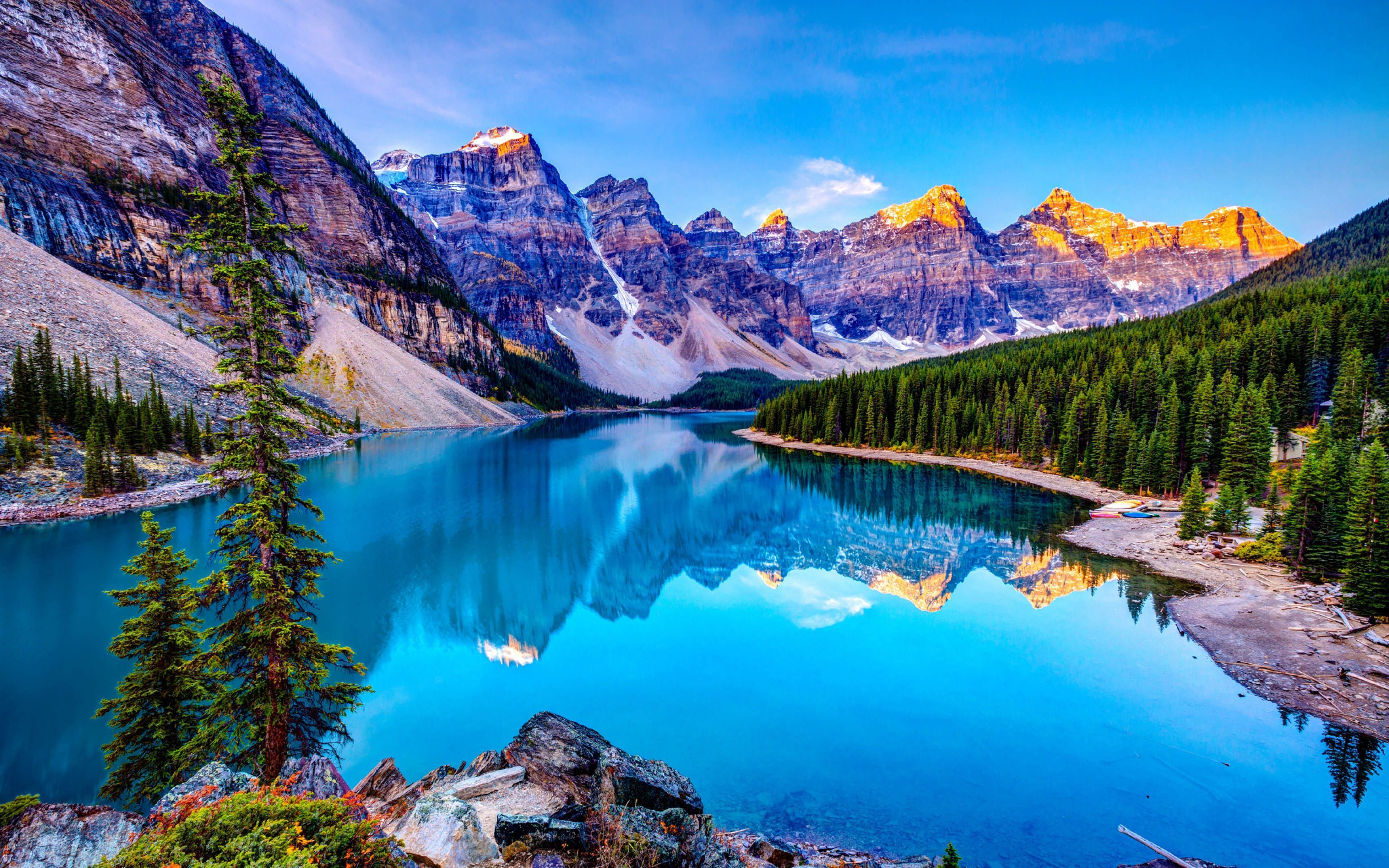 Stunning 4K wallpaper of a pristine turquoise lake nestled amidst snow-capped mountains and lush evergreen forests
