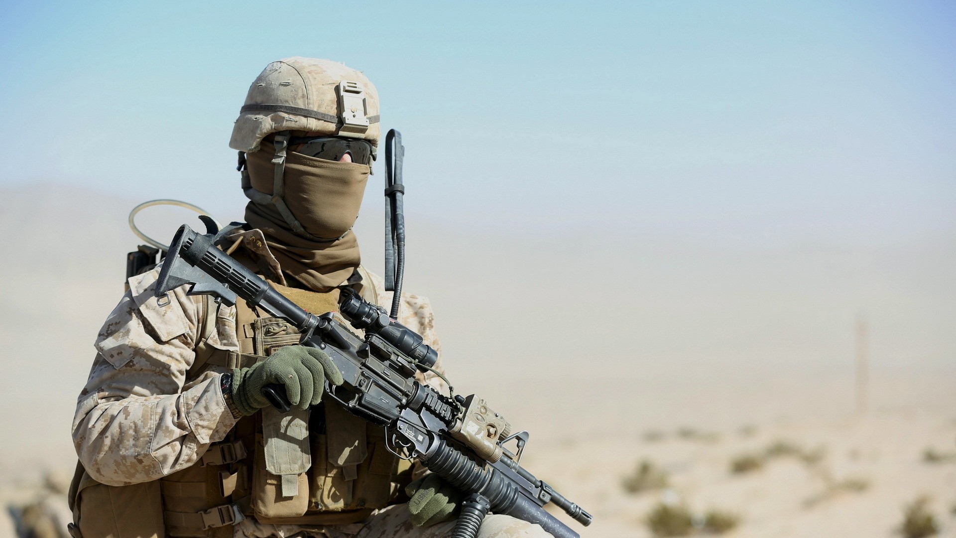 A soldier in desert camouflage holds a rifle, likely in a desert training exercise