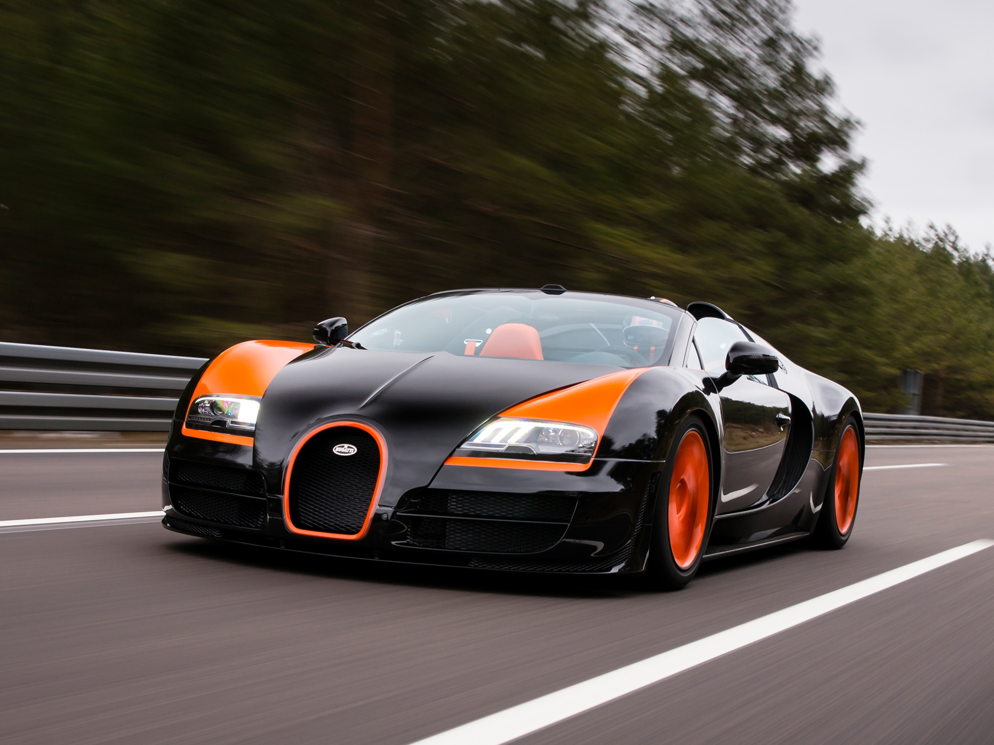A black and orange Bugatti Veyron Grand Sport speeds down a racetrack, showcasing its sleek design and powerful performance
