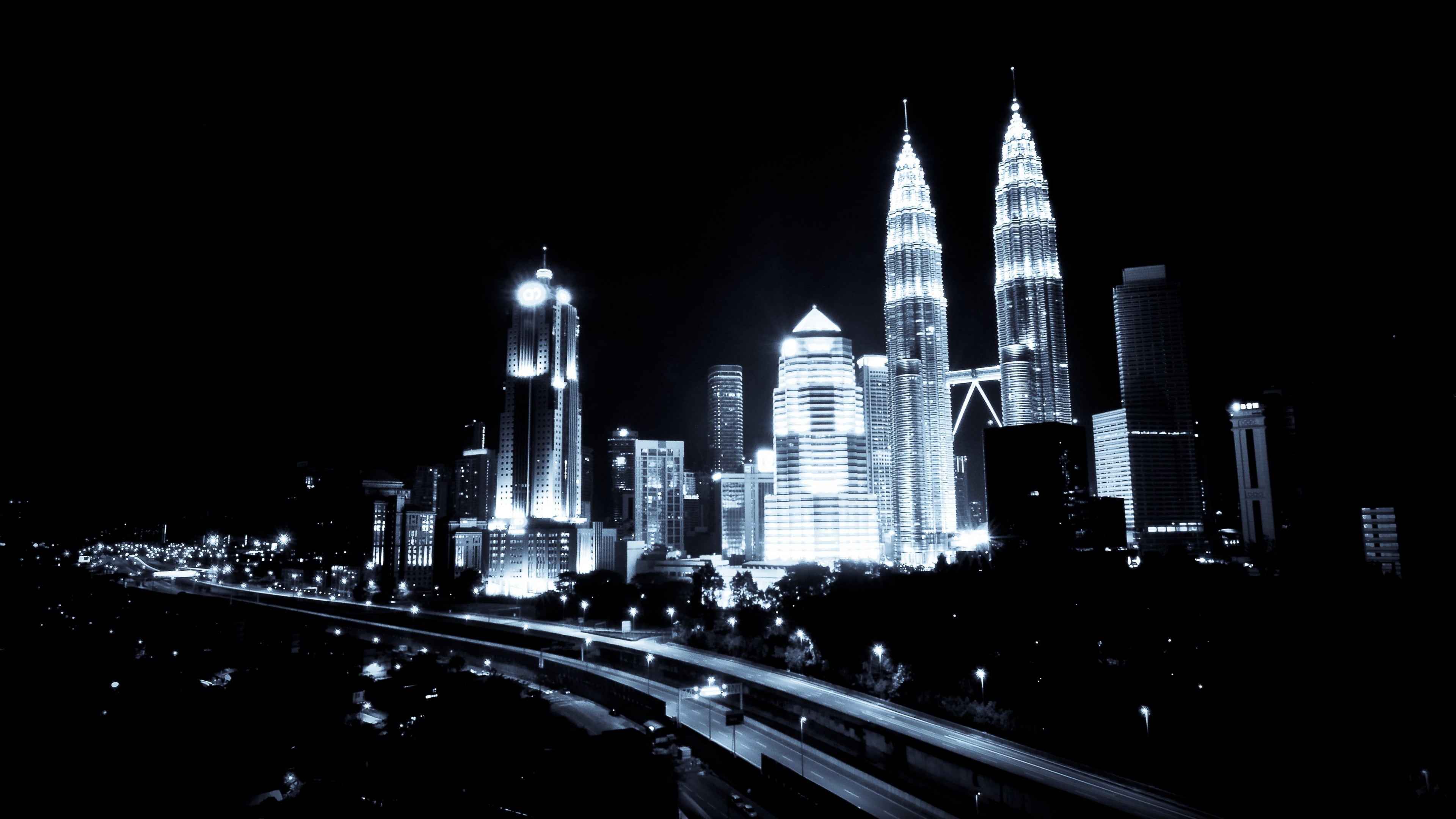 A stunning black and white night view of the Kuala Lumpur city skyline with illuminated skyscrapers and light trails from traffic
