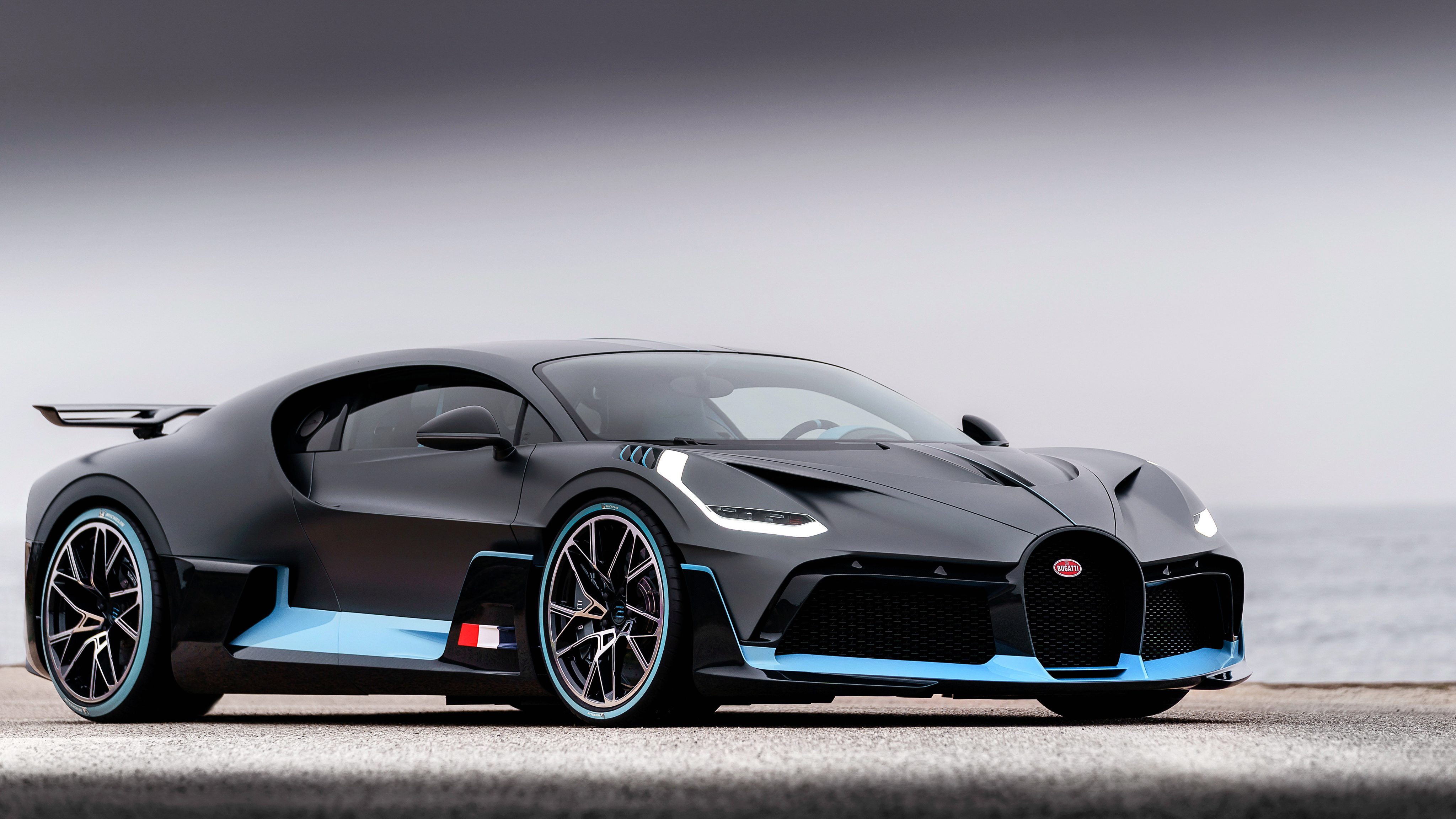 A sleek, black Bugatti hypercar with light blue accents, parked by the sea