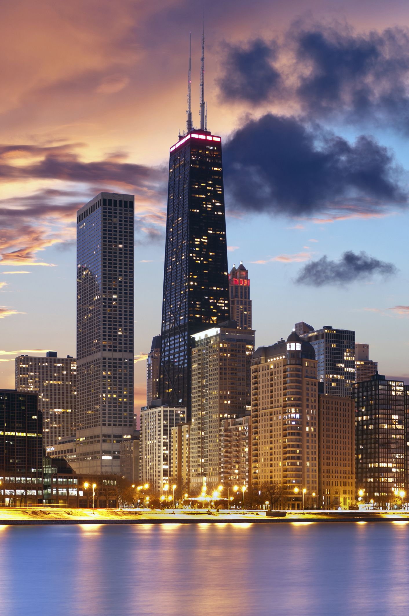 A stunning twilight view of the Chicago skyline, featuring the iconic John Hancock Center, reflected in the calm waters of Lake Michigan