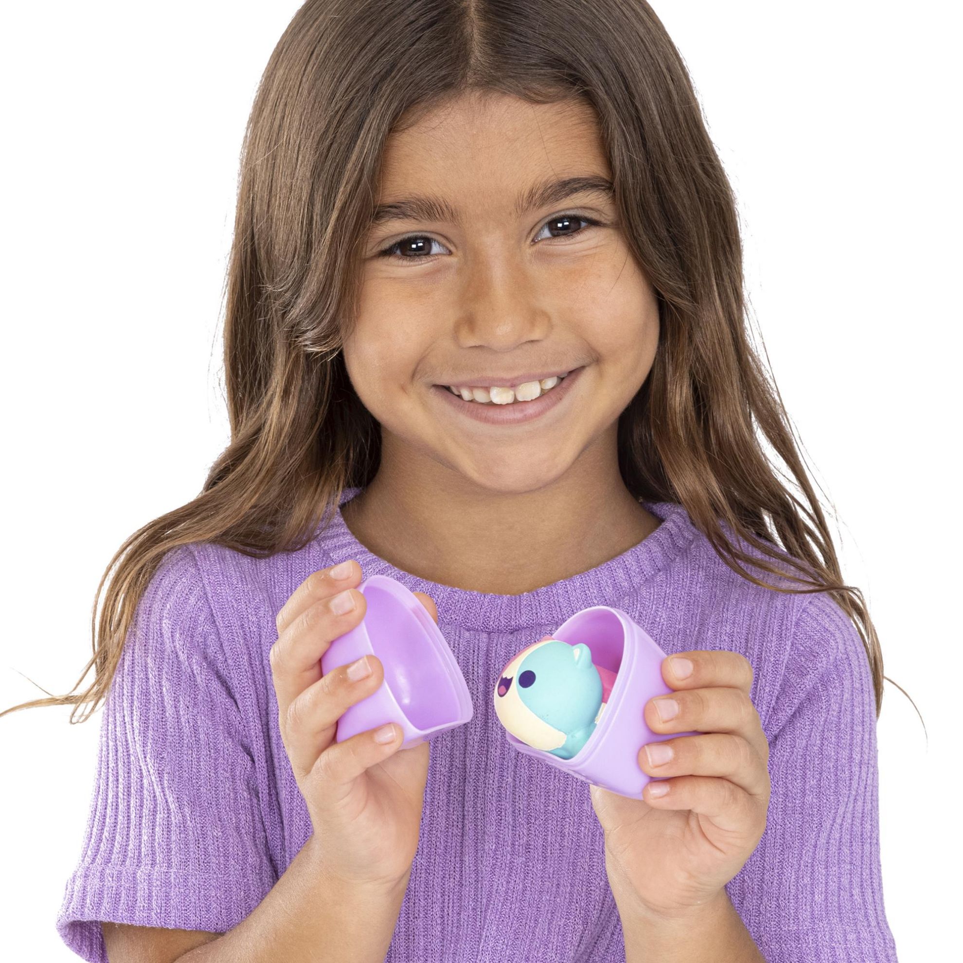 A young girl smiles while holding a purple toy egg containing a small plush animal