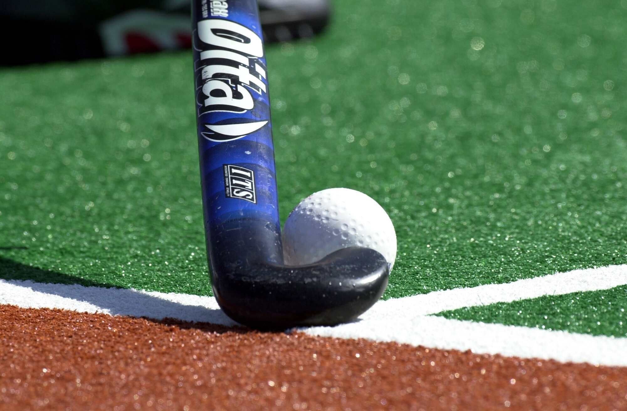 Close-up of a field hockey stick and ball on the field, highlighting the equipment and the sport