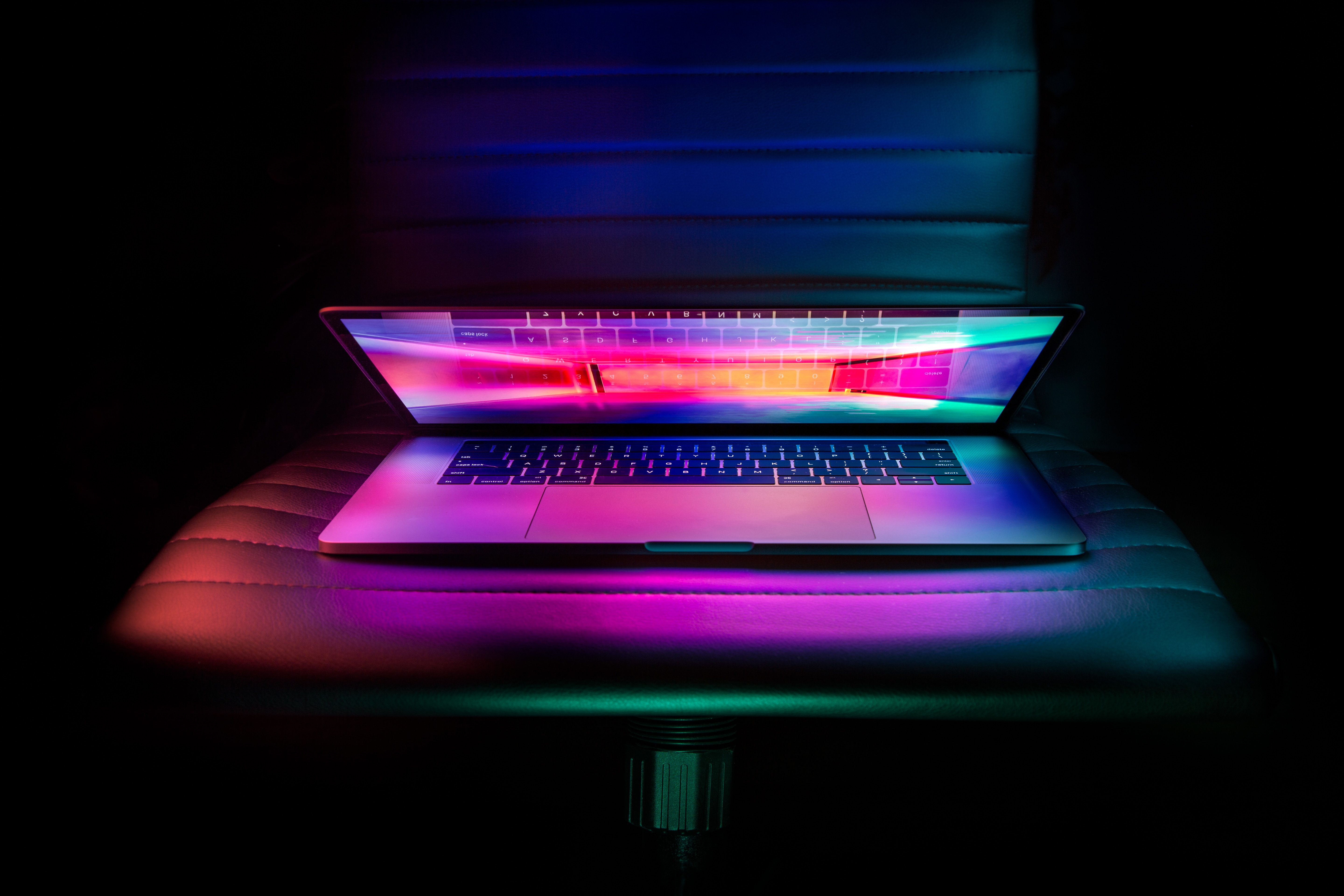 A laptop with a vibrant, colorful keyboard and screen reflection, set against a dark background