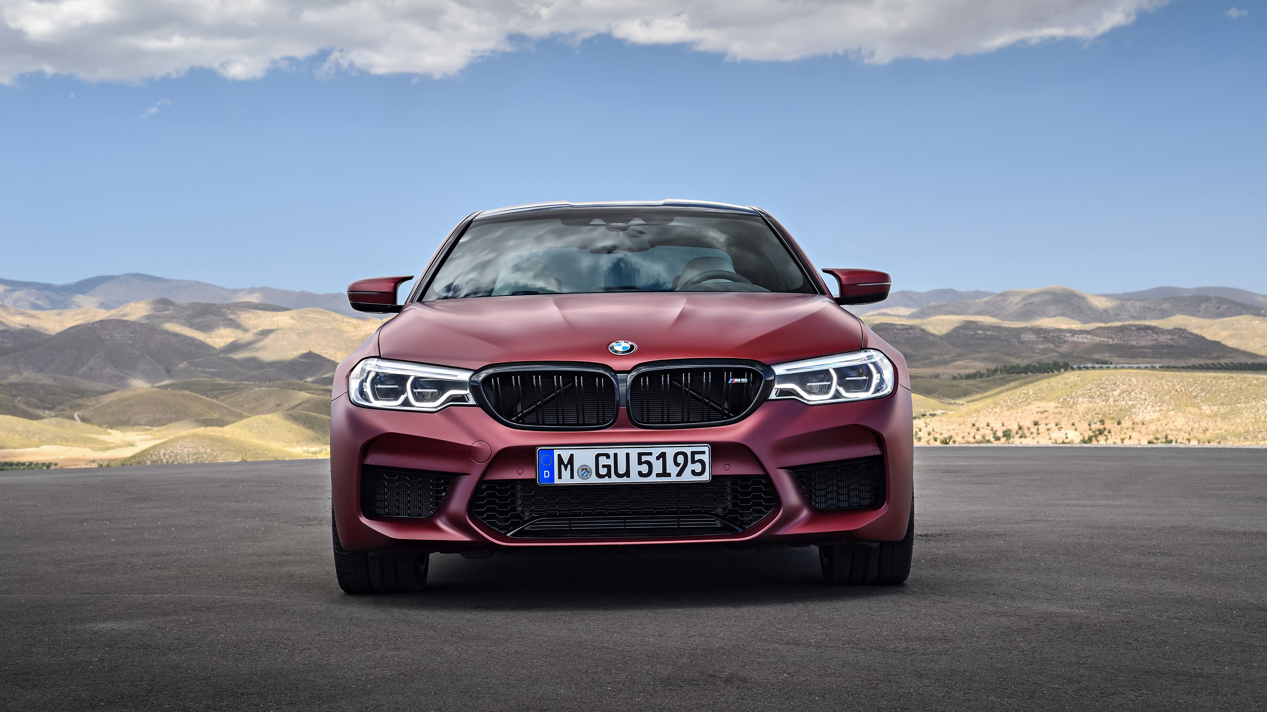Red BMW M5 parked on a paved surface with mountains in the background
