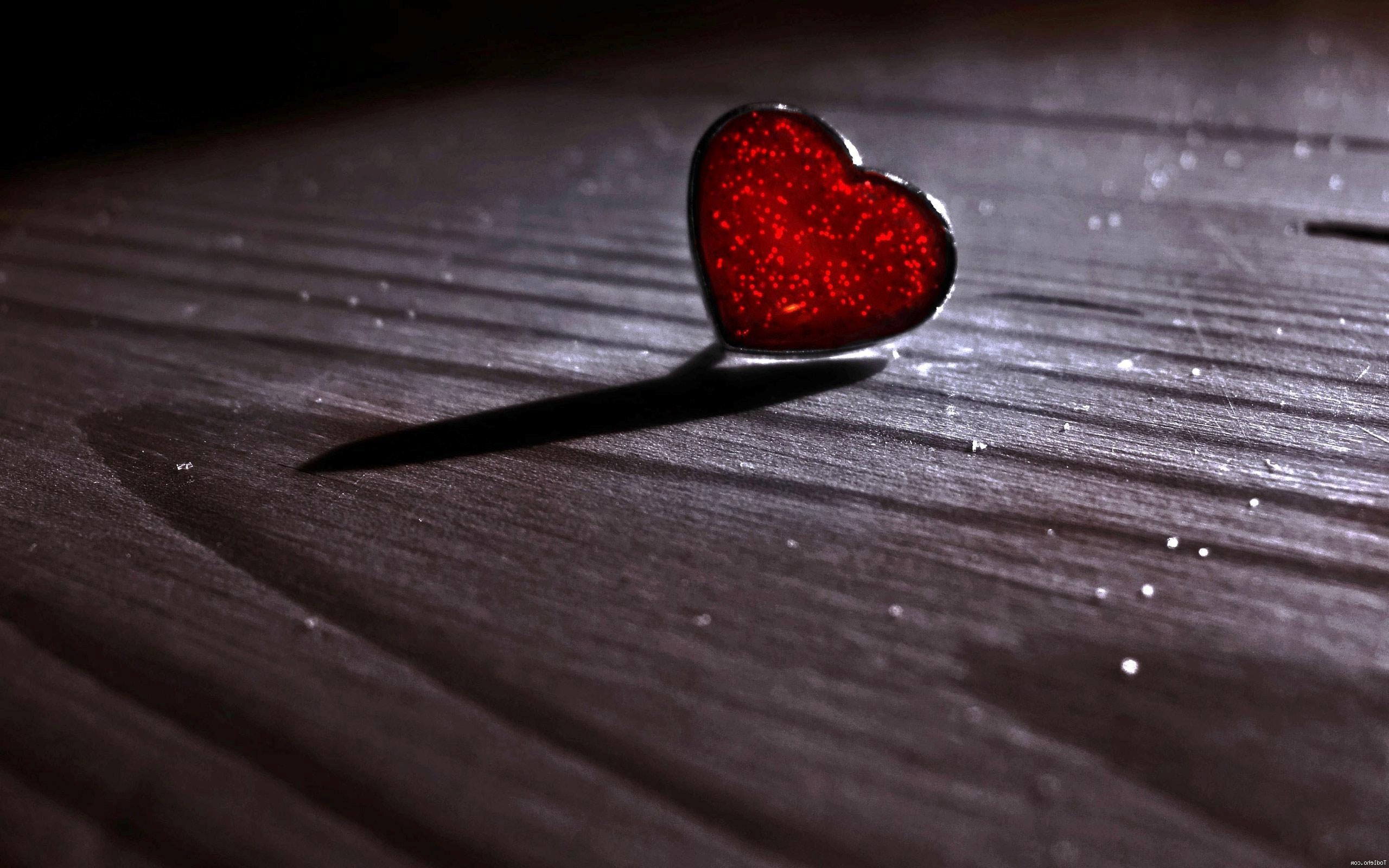 A glistening red heart ornament casts a dramatic shadow on a dark wooden surface, evoking feelings of love, romance, and Valentine's Day