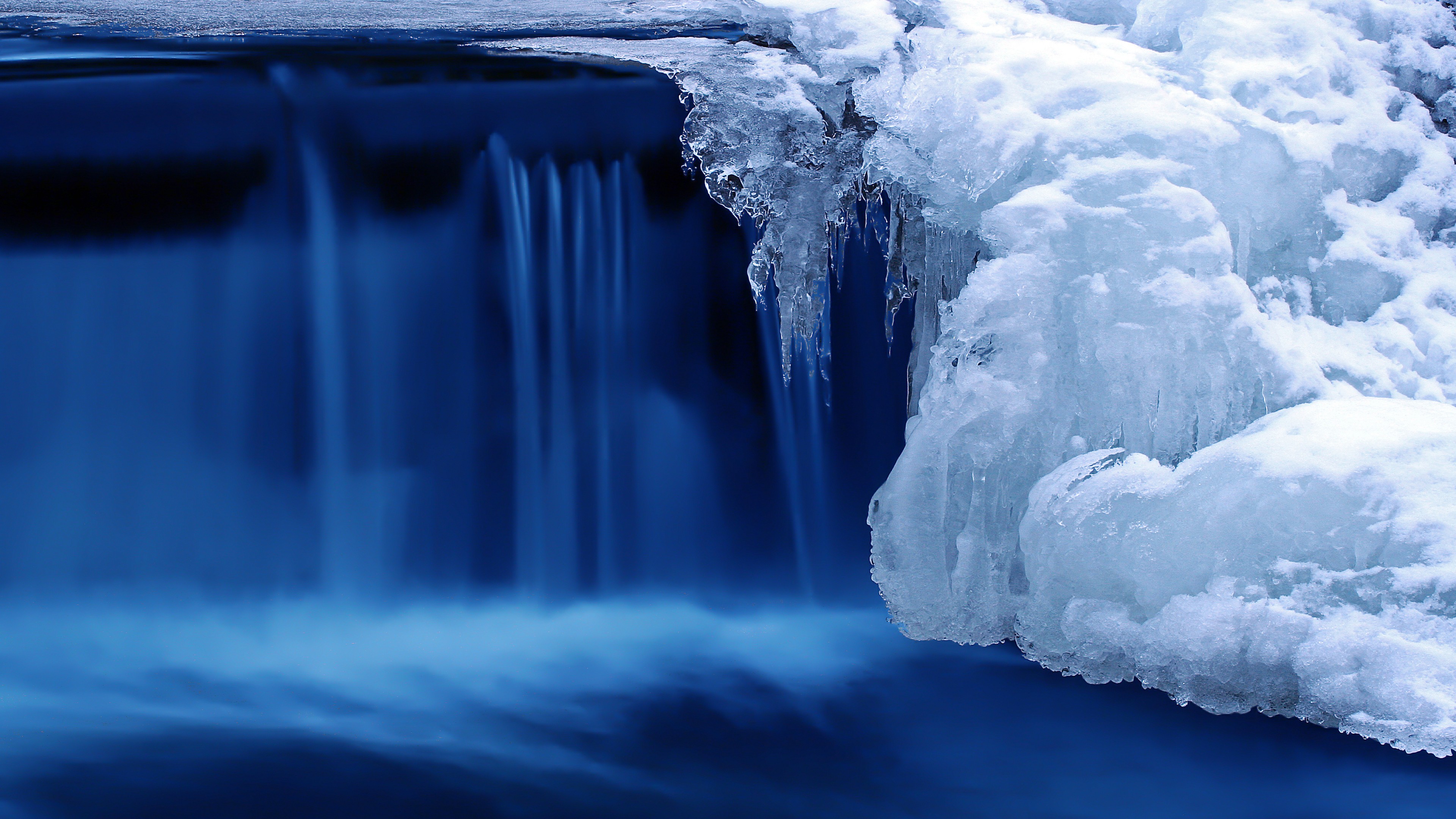 Close-up of a partially frozen waterfall, showcasing the contrast between the flowing blue water and the icy formations