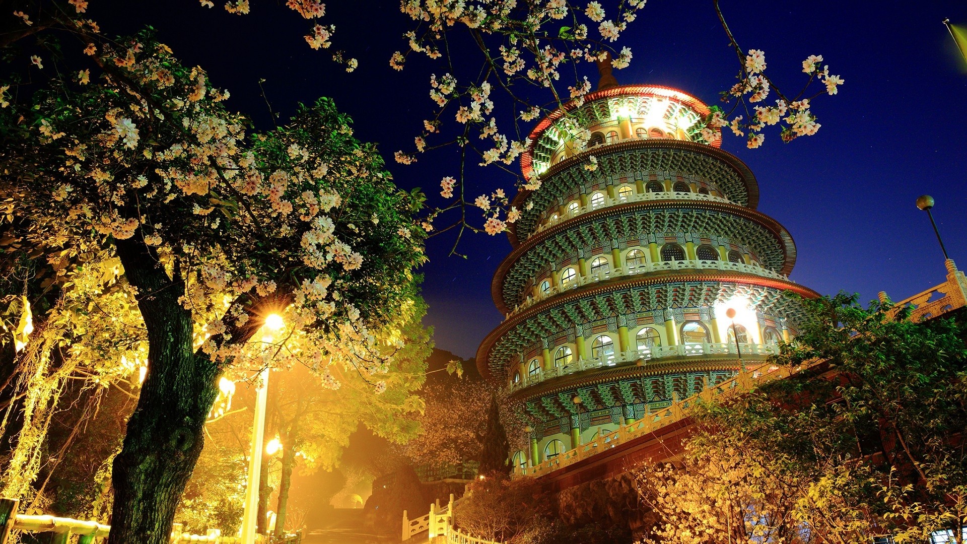 A vibrant night scene of Ci'en Pagoda in Taiwan, illuminated against a dark blue sky, with cherry blossoms in the foreground