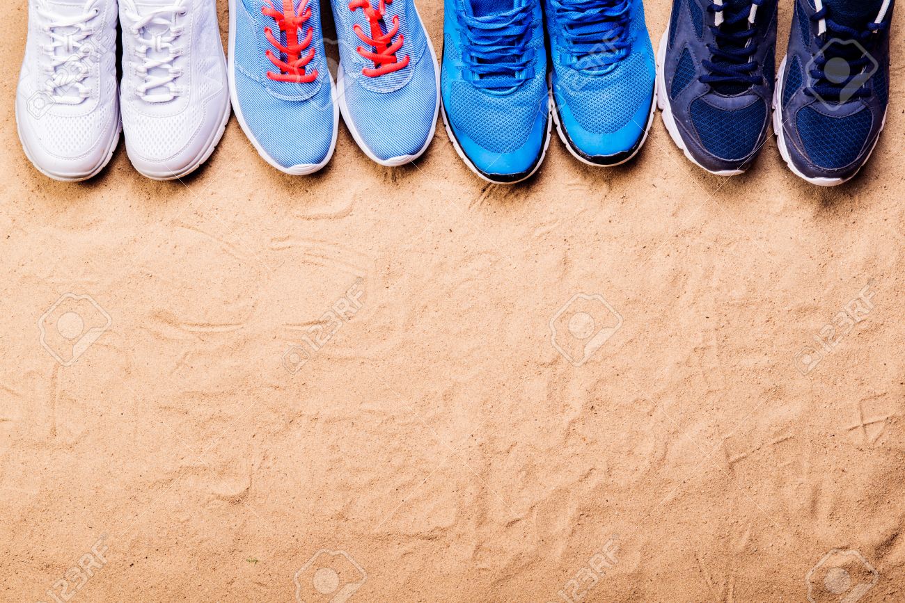 Various Sports Shoes In A Row Against Sand Background Studio
