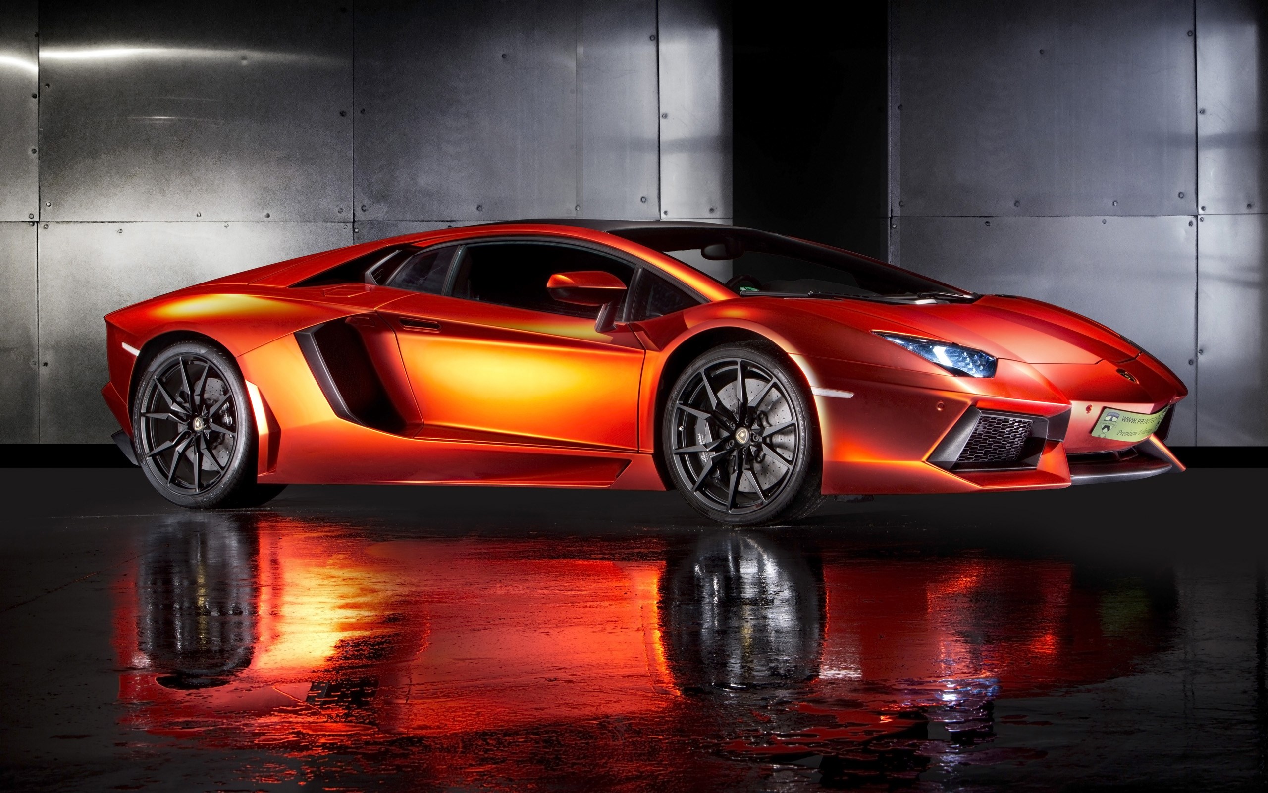 A vibrant orange Lamborghini Aventador sports car parked on a wet, reflective surface, possibly in a showroom or garage