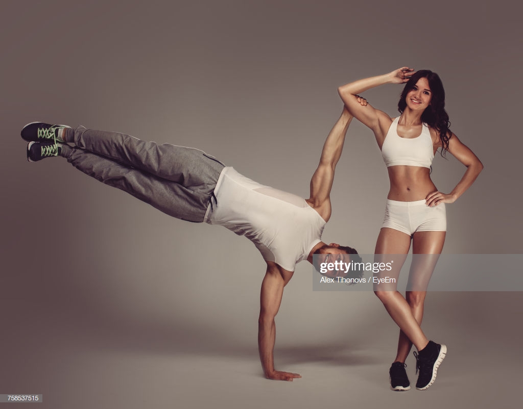 Portrait Of Young Athletic Couple Practicing Acroyoga Against Gray