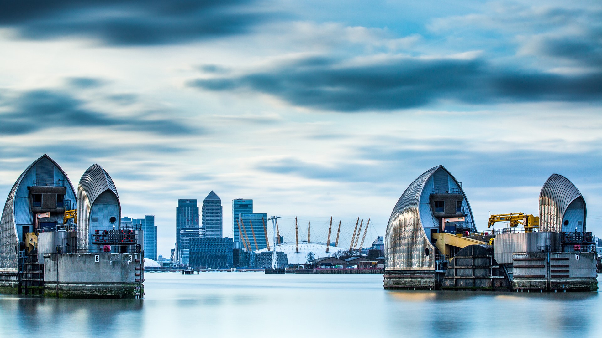 Thames Barrier On River And Canary Wharf In The Background