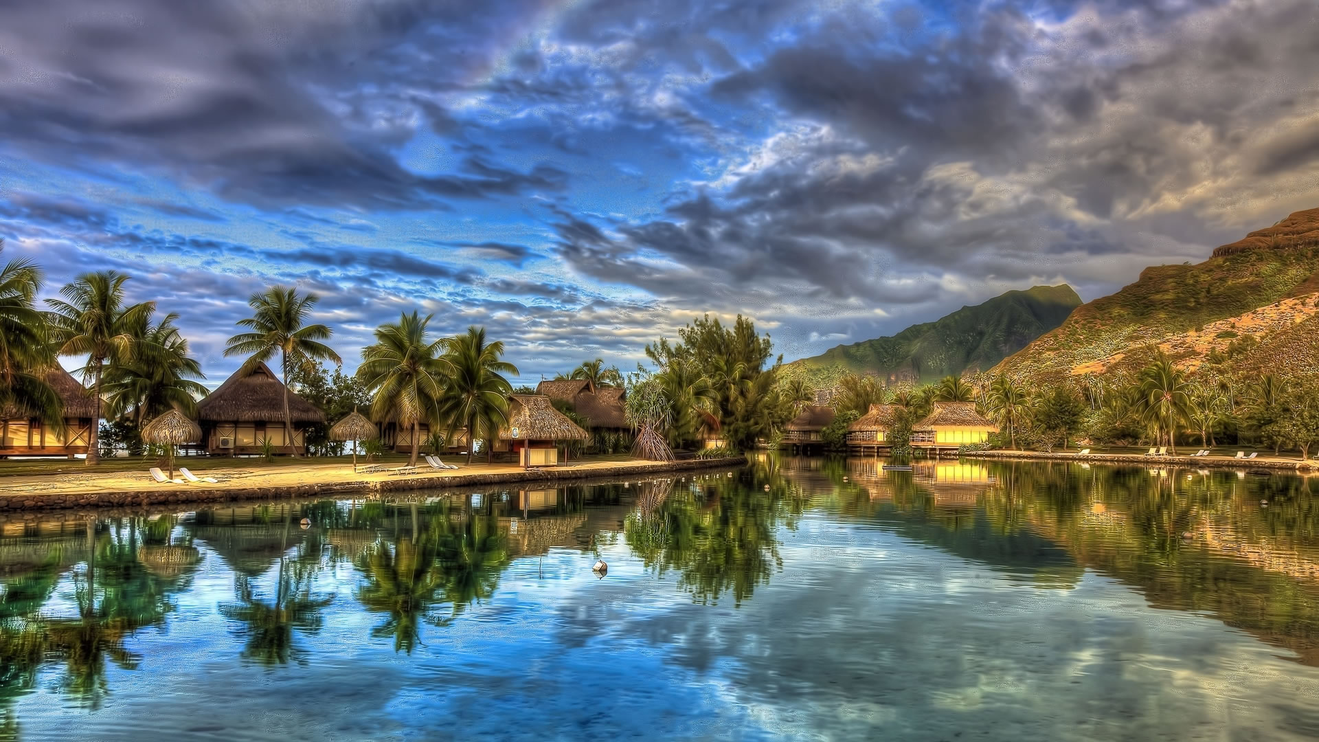 Tranquil summer scene with overwater bungalows, palm trees, and a calm lagoon reflecting the colorful sunset sky