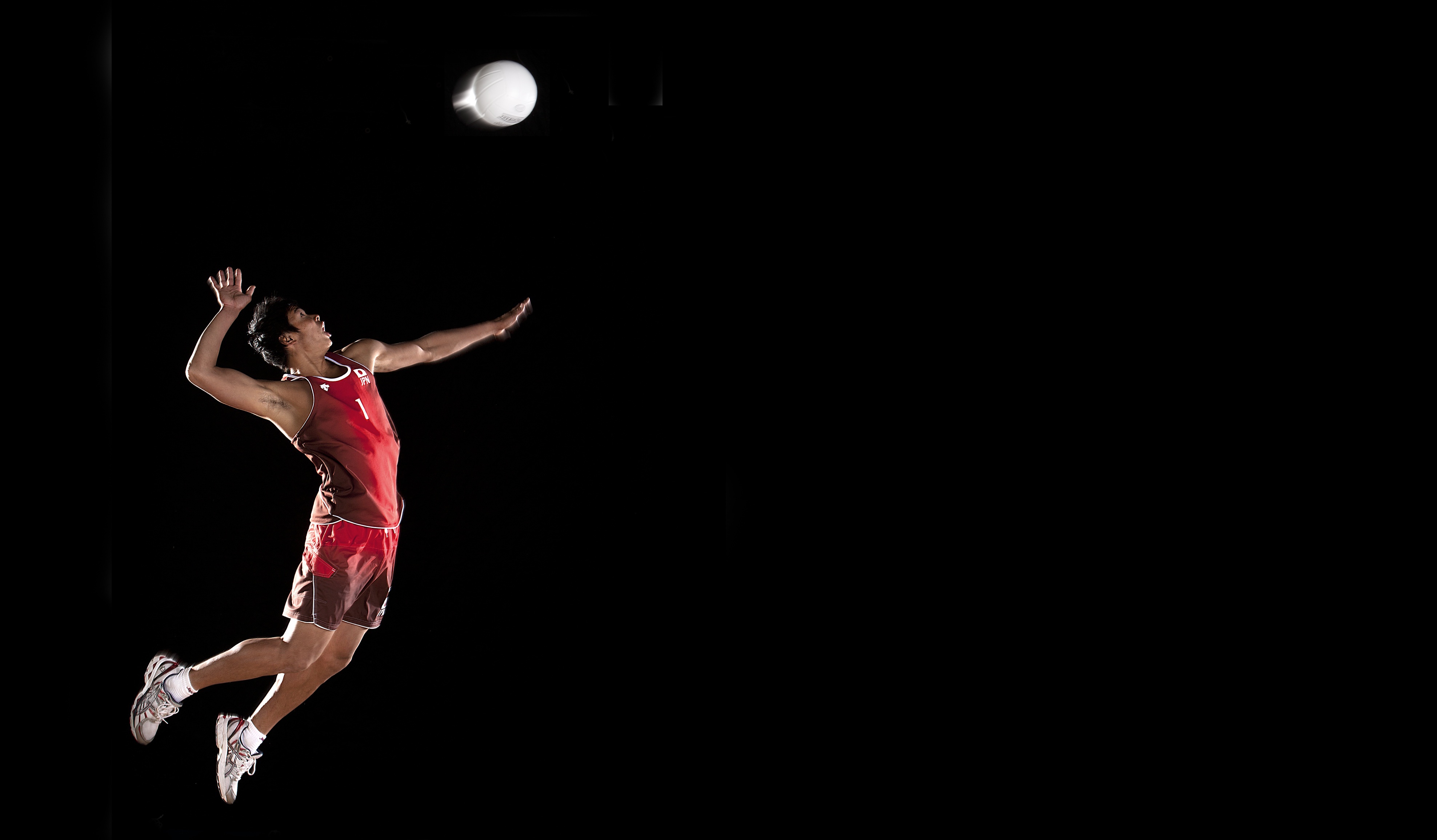A volleyball player jumps high in the air to spike the ball against a black background