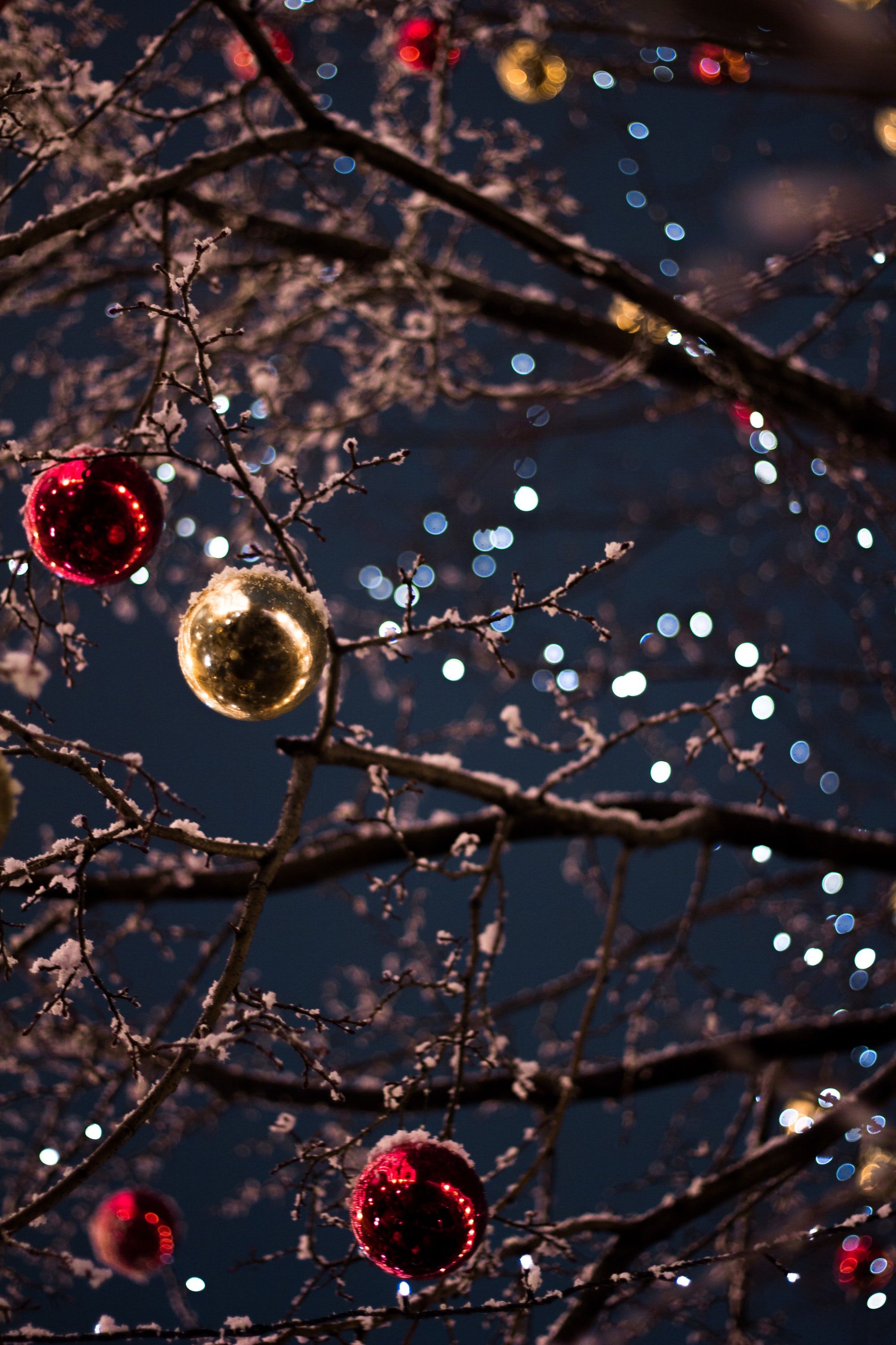 Christmas ornaments hanging on a snow-dusted tree at night, lit by twinkling fairy lights. A preppy and festive 4k wallpaper