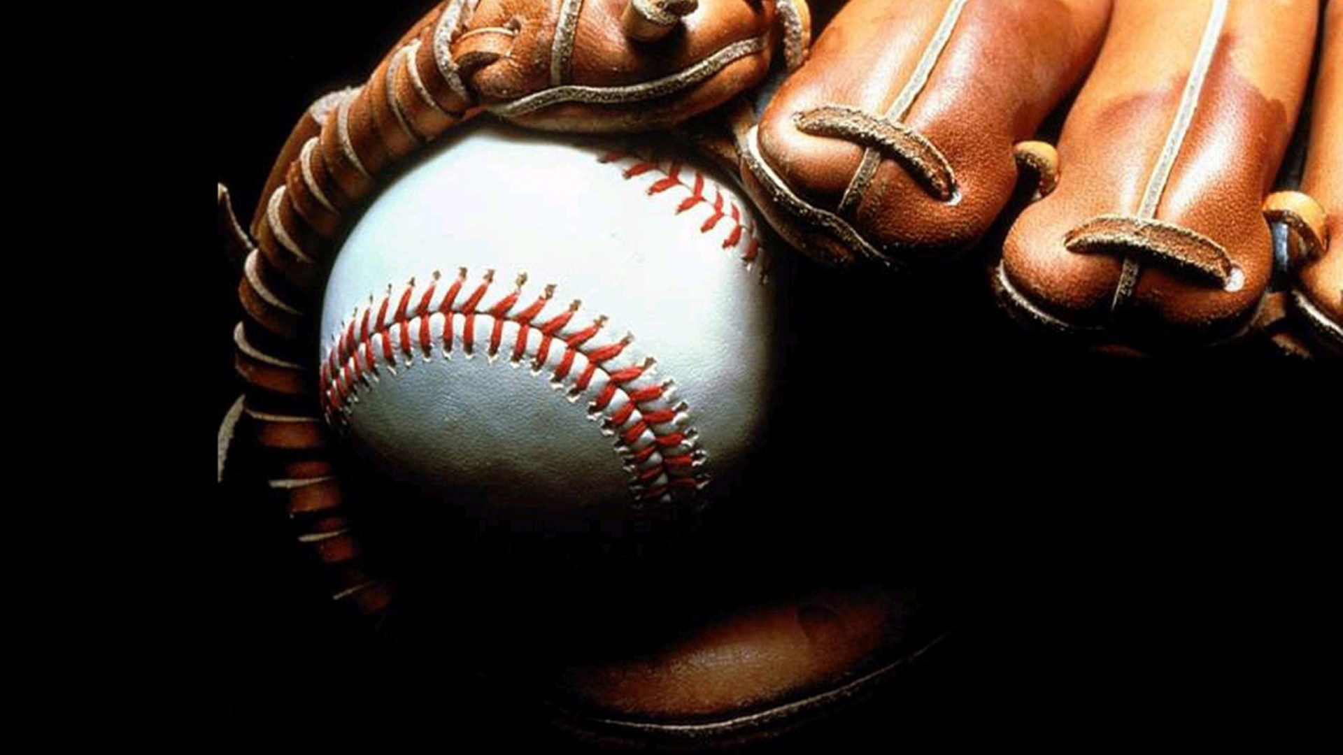 Close-up of a baseball nestled in a worn leather glove, highlighting the texture of the ball and glove against a dark background