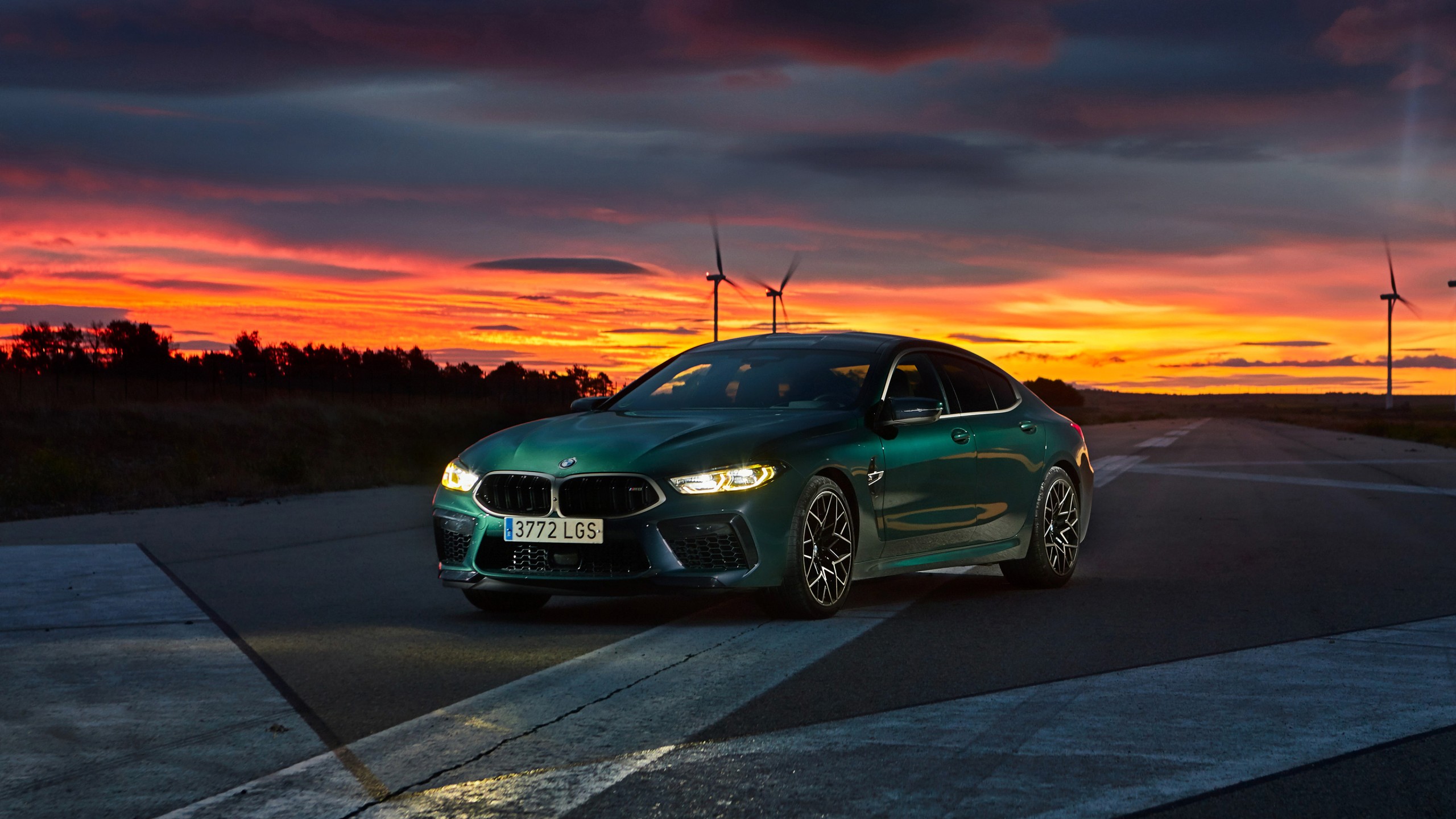 A sleek, green BMW 8 Series Gran Coupe against a vibrant sunset backdrop