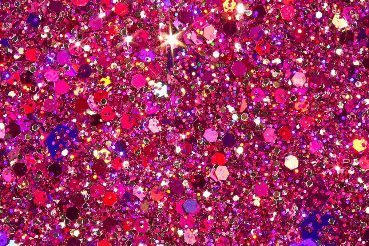 A close-up view of vibrant pink glitter, showcasing a mix of shapes and sizes, reflecting light and creating a sparkly, textured background