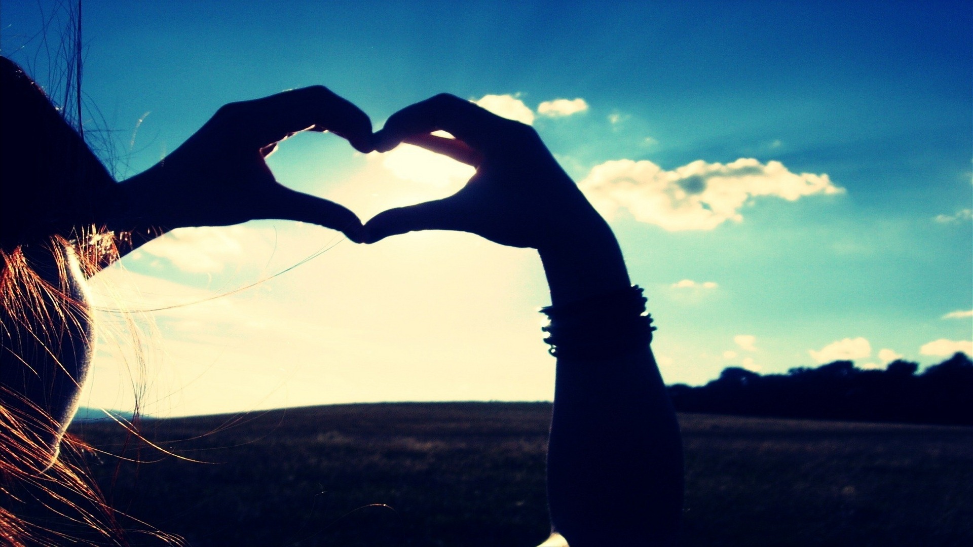 Silhouetted hands form a heart shape against a vibrant sunset backdrop, symbolizing love and romance
