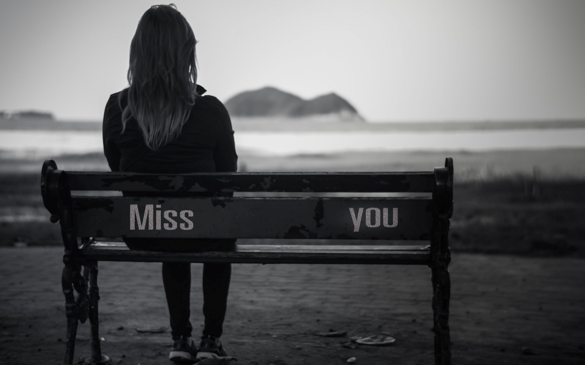 A grayscale image of a woman sitting alone on a bench with the words 'Miss You' inscribed on it, conveying a sense of longing and sadness