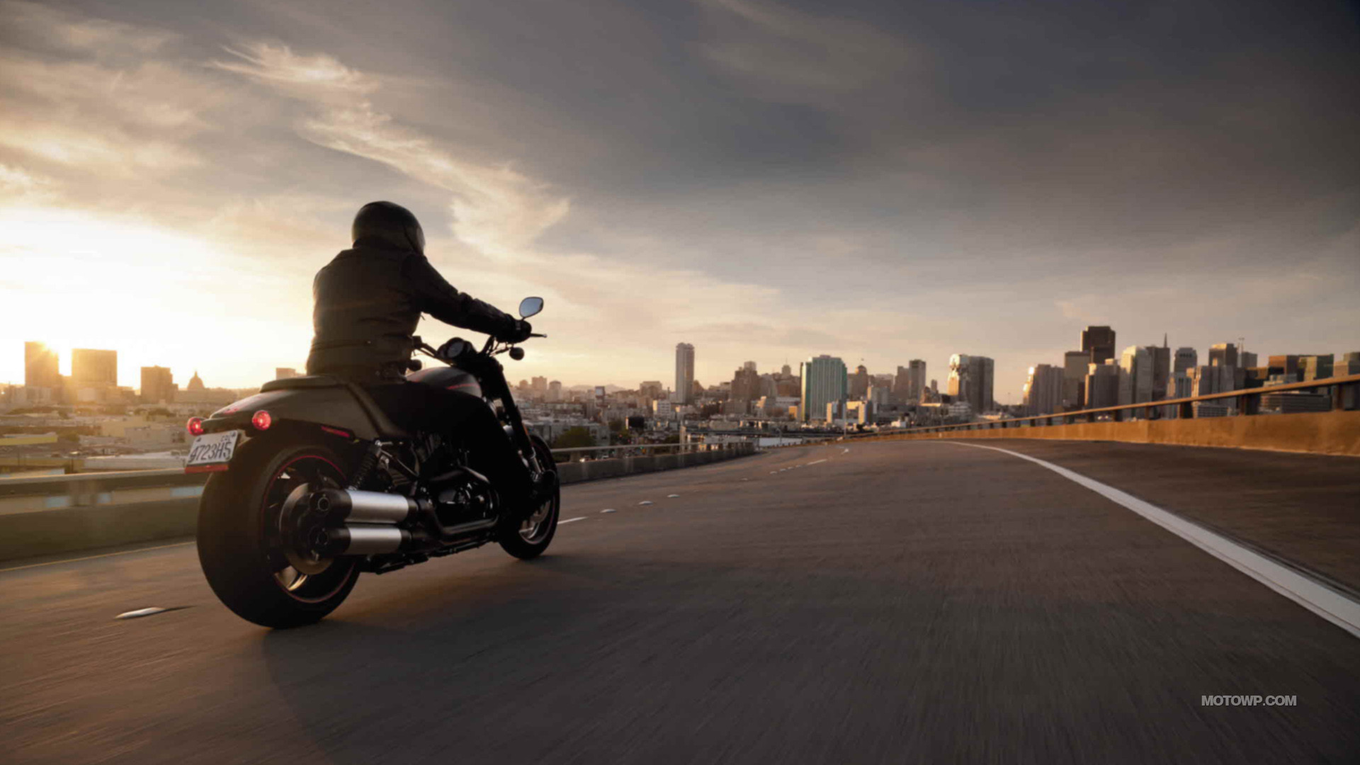 A Harley Davidson motorcycle cruising towards a city skyline at sunset