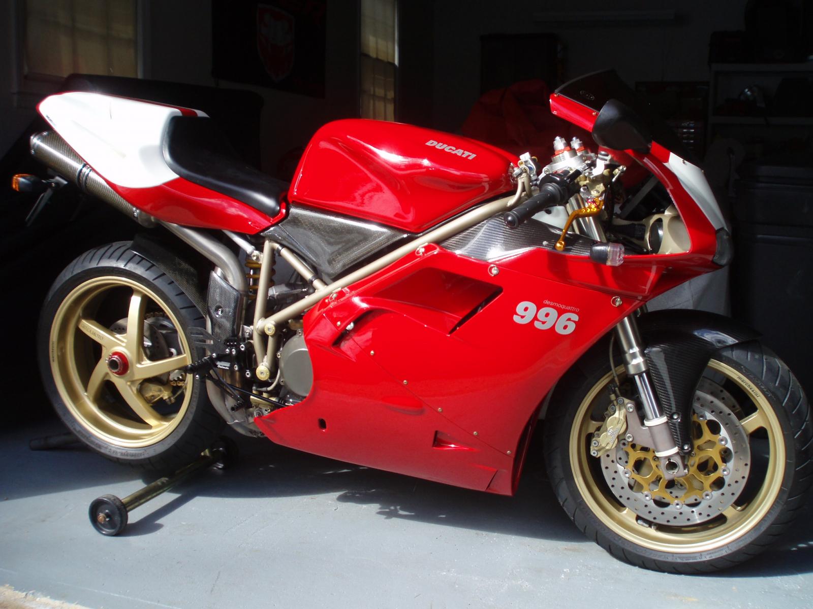 Ducati 996 sportbike in red and white, parked in a garage. This image highlights the bike's sleek design, gold Marchesini wheels, and carbon fiber accents