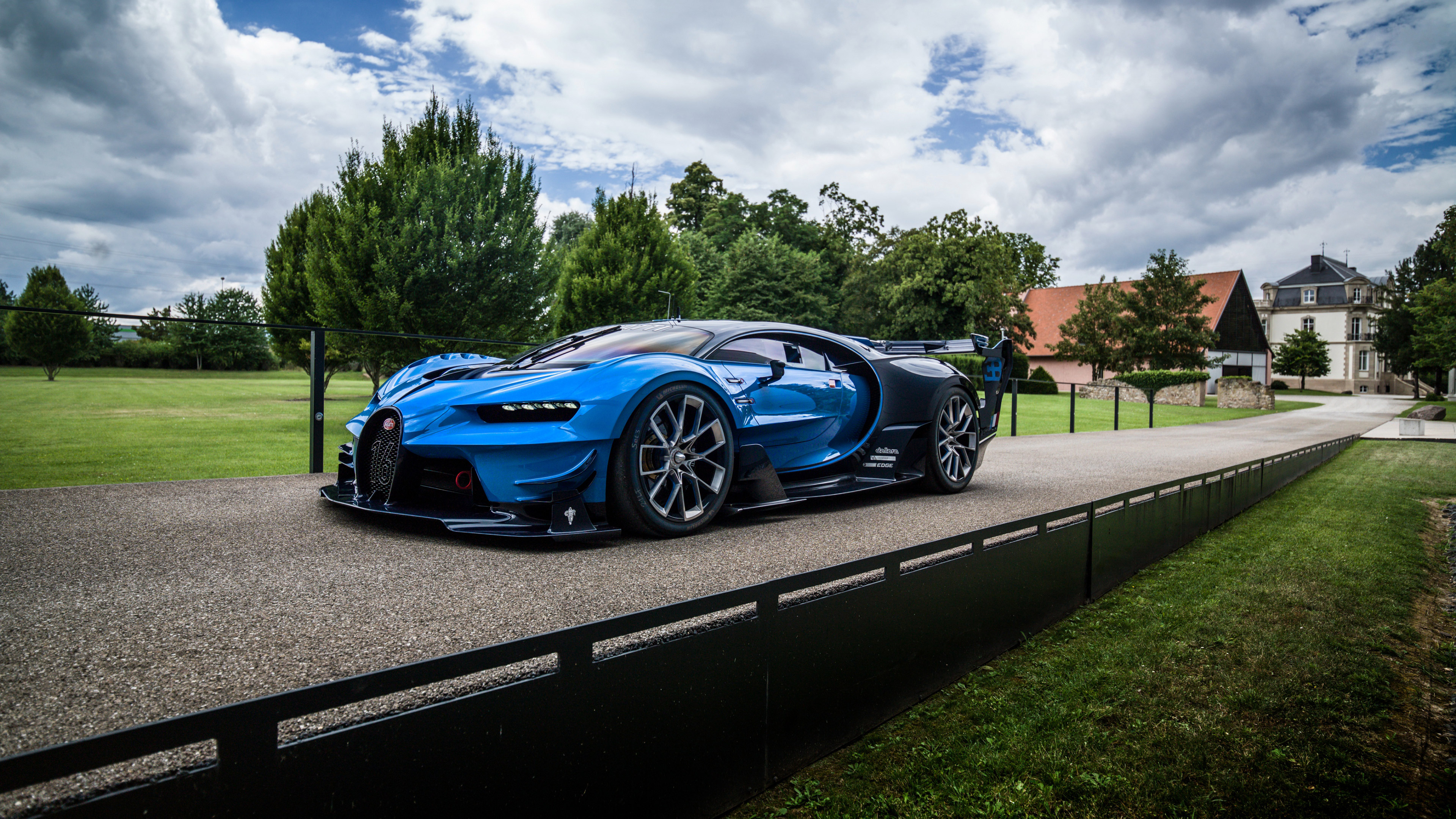 A sleek, futuristic blue Bugatti Vision Gran Turismo parked on a driveway with a classic French chateau in the background