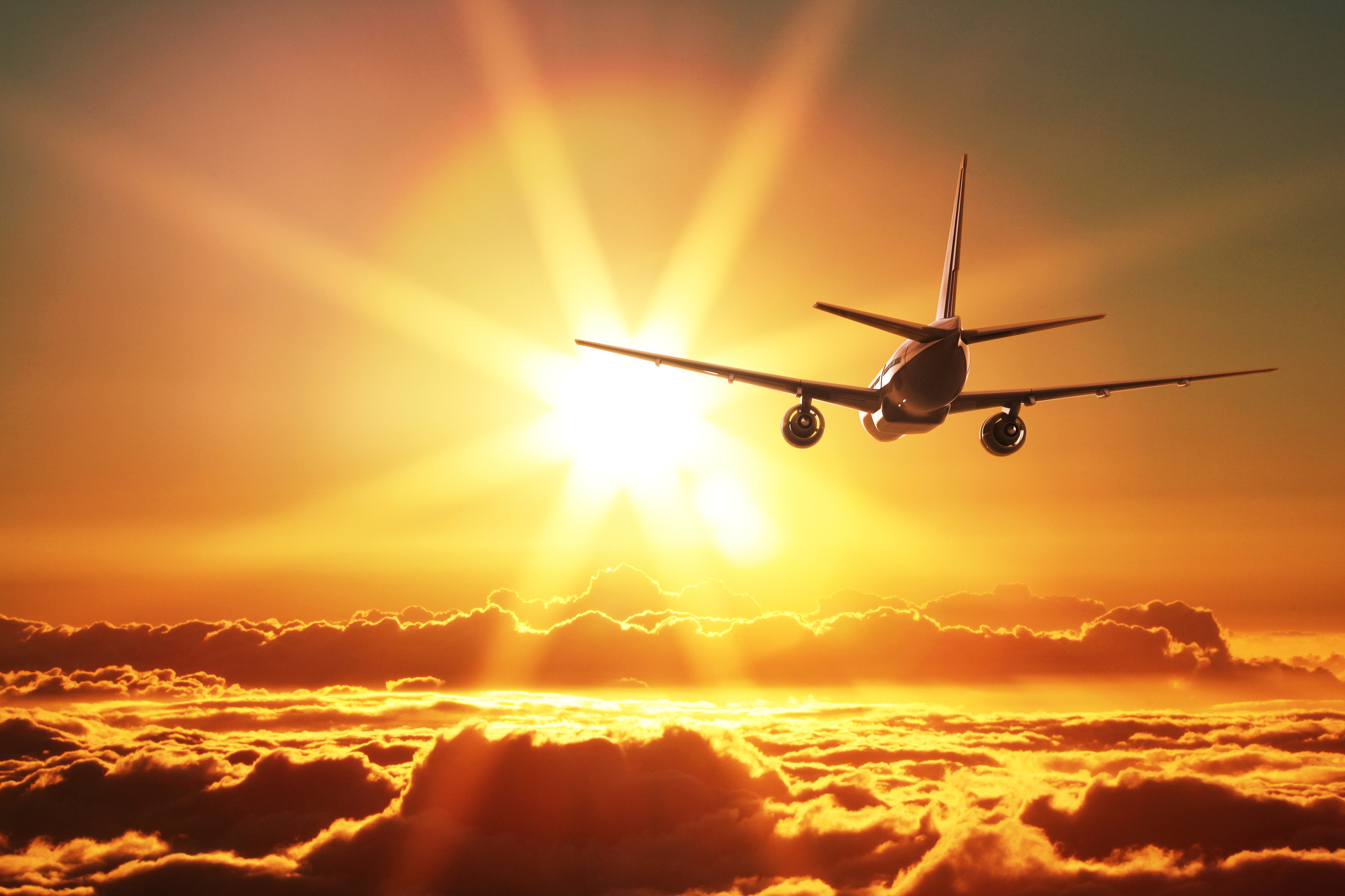 A passenger airplane soaring through a vibrant sunset sky above a layer of clouds